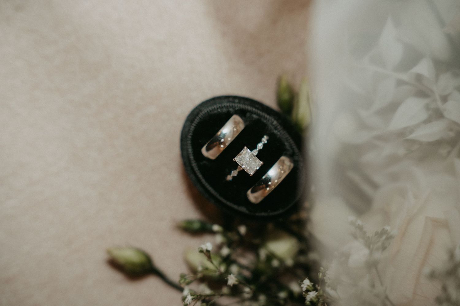 A collection of black and white wedding rings displayed with delicate greenery and floral accents on a light surface.