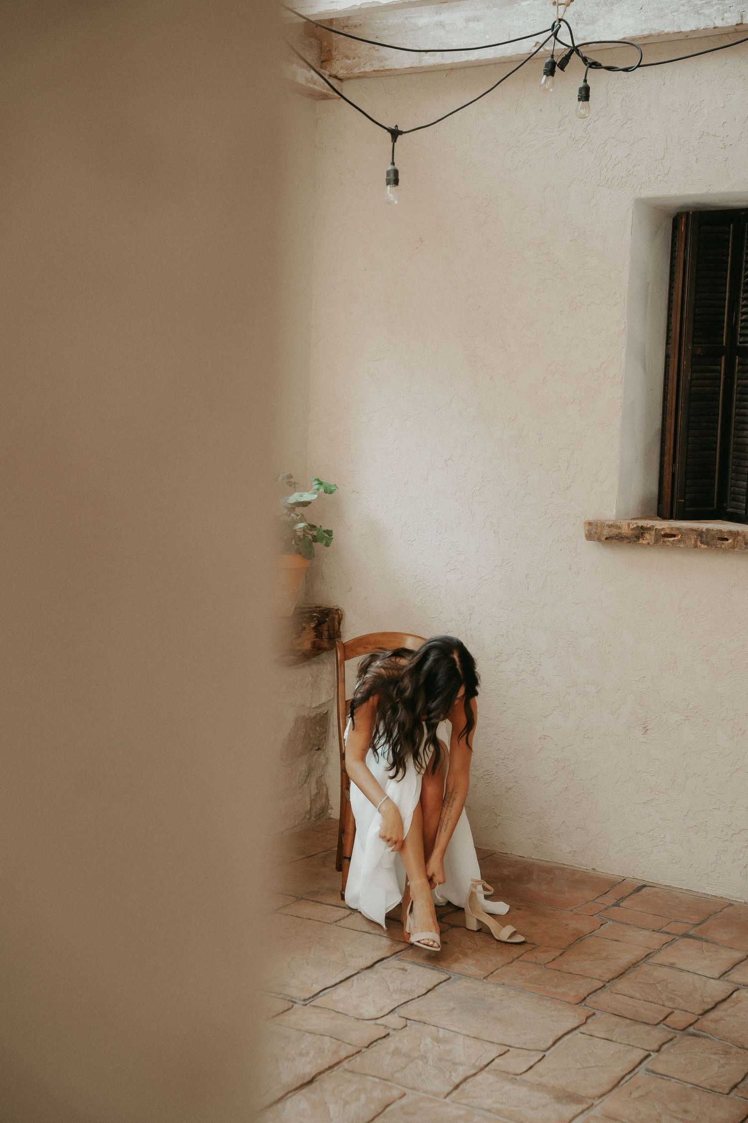 Person in white dress sitting alone on tiled floor against white wall with dramatic lighting.