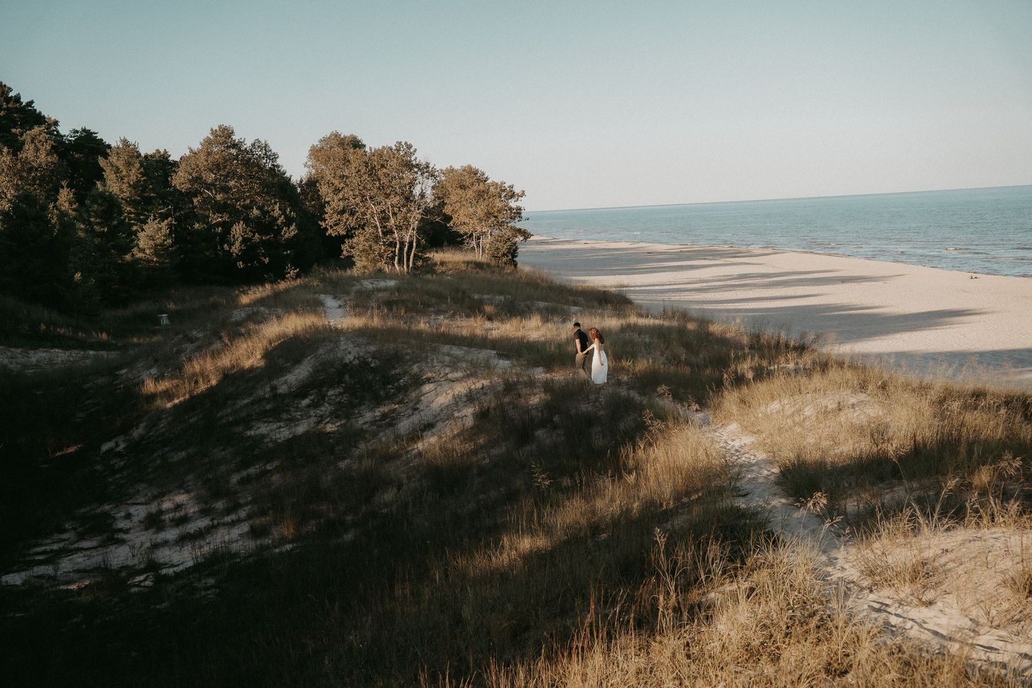 A serene coastal landscape with rolling sand dunes and beach grass overlooking the ocean at sunset.