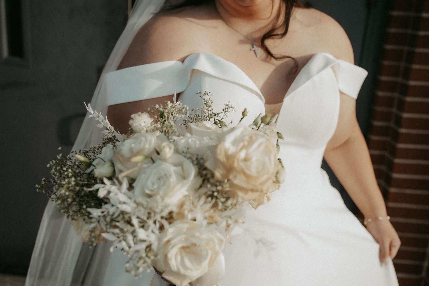 A delicate white bridal bouquet featuring roses, baby's breath, and greenery against a wedding dress.