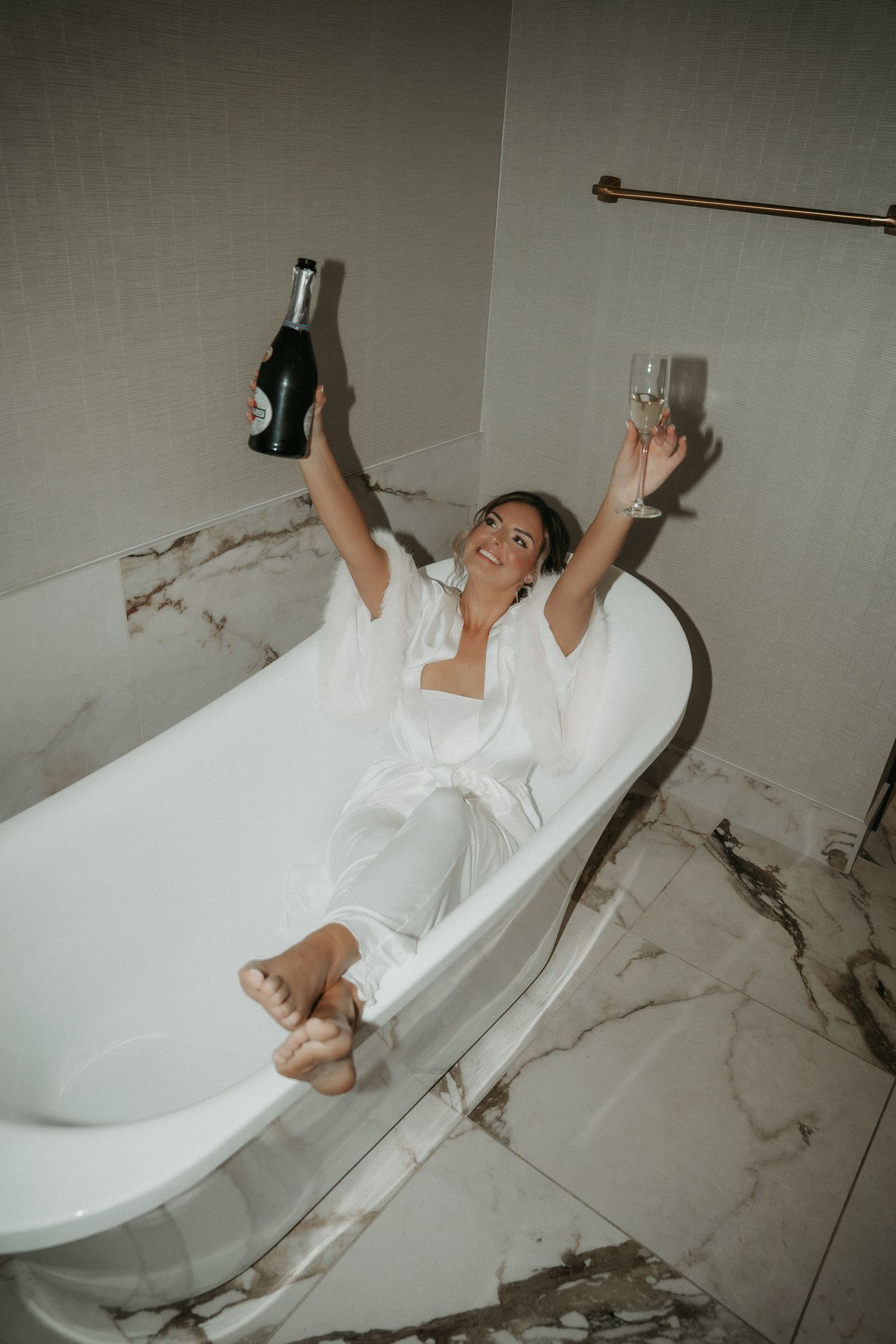A person in a white bathrobe relaxes in a luxurious marble bathroom with a freestanding tub.
