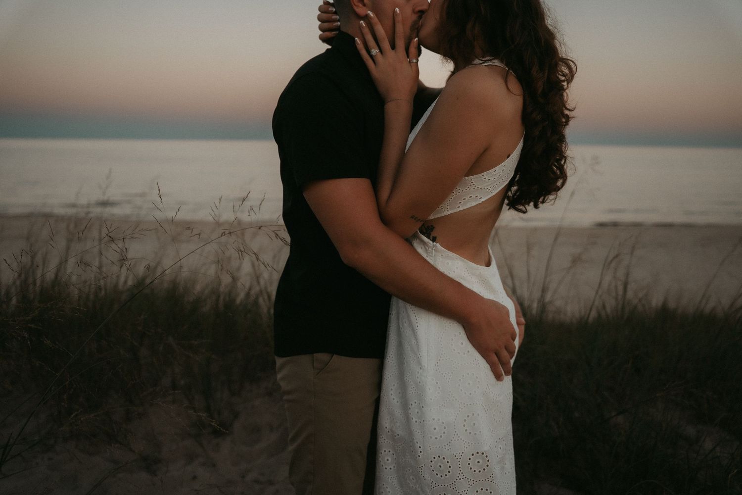 A romantic couple embraces during sunset at a beach, silhouetted against the warm evening sky.