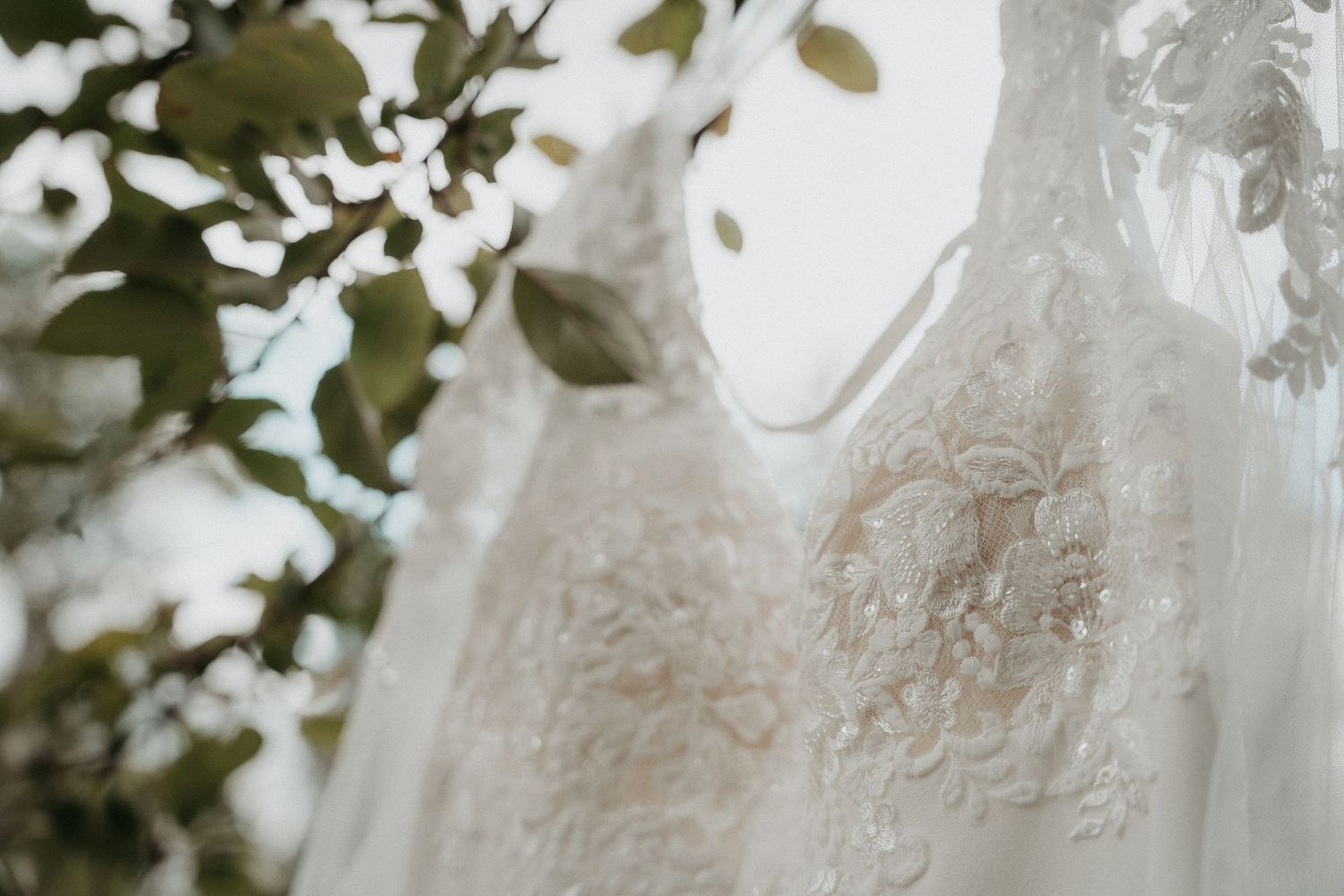 A romantic wedding couple embraces under a floral arch with white roses and greenery at an outdoor ceremony.