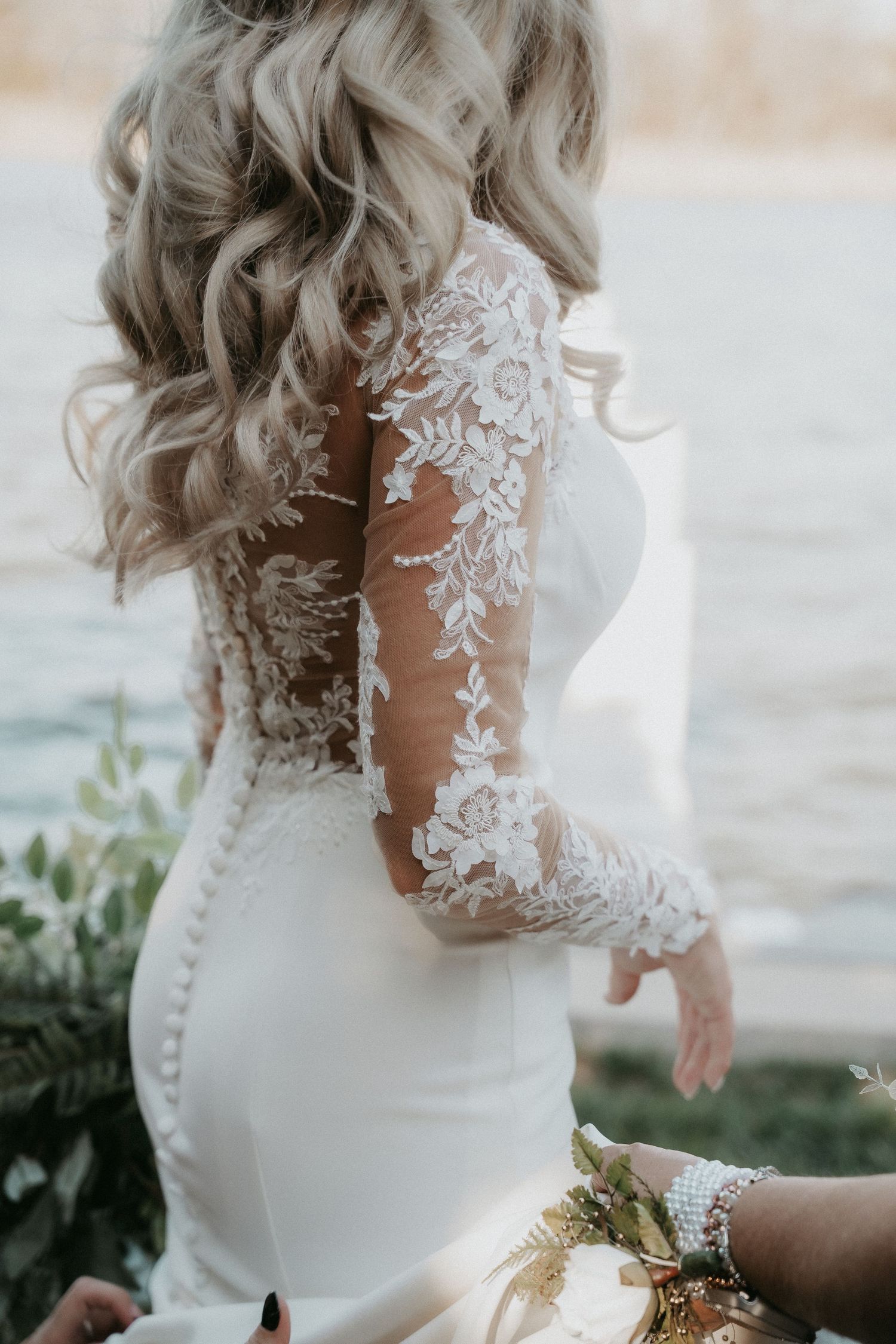 Close-up details of a bride's wedding dress showing delicate lace sleeves and button details on the back.
