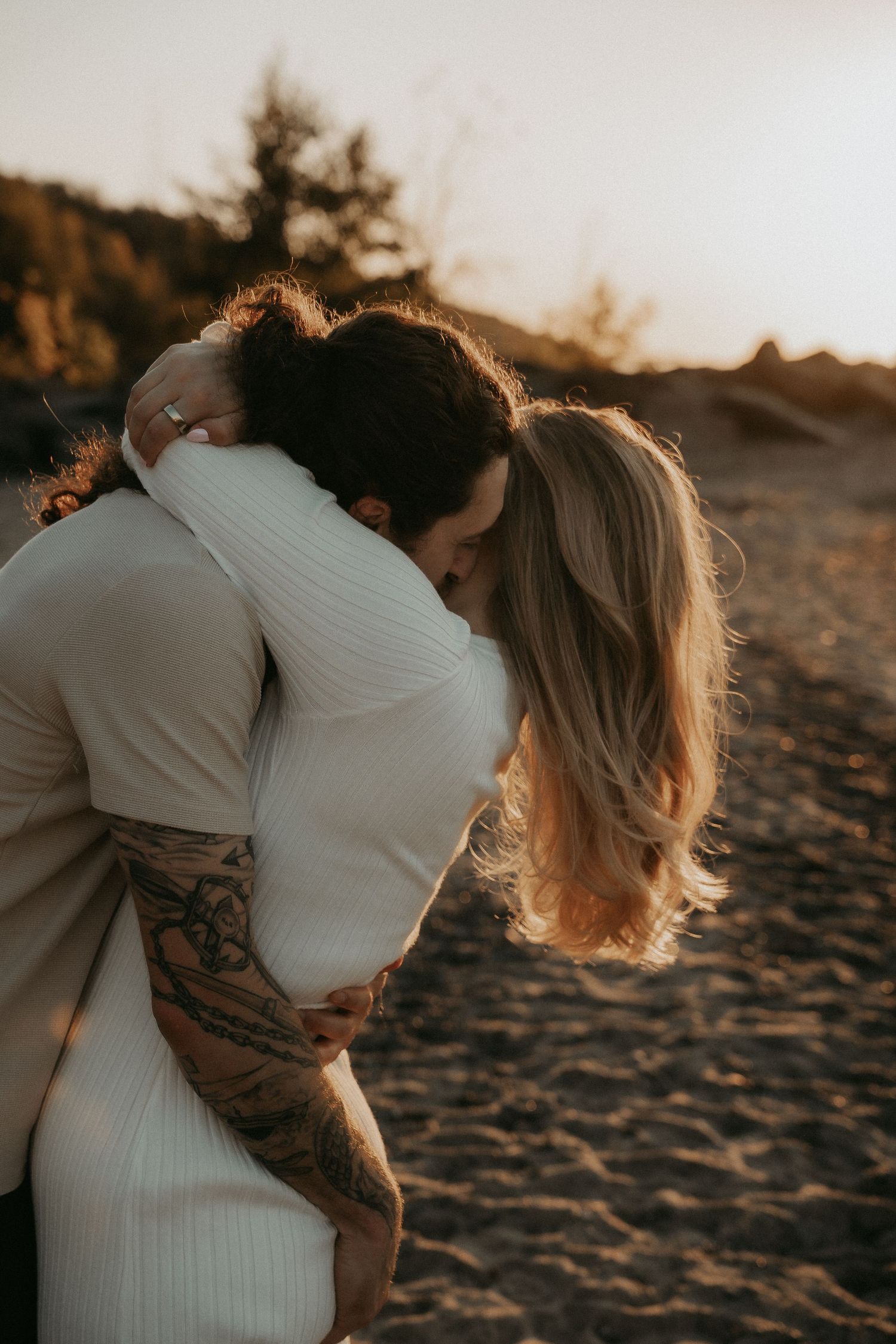 Romantic couple embracing on a sandy beach at sunset in warm golden light.