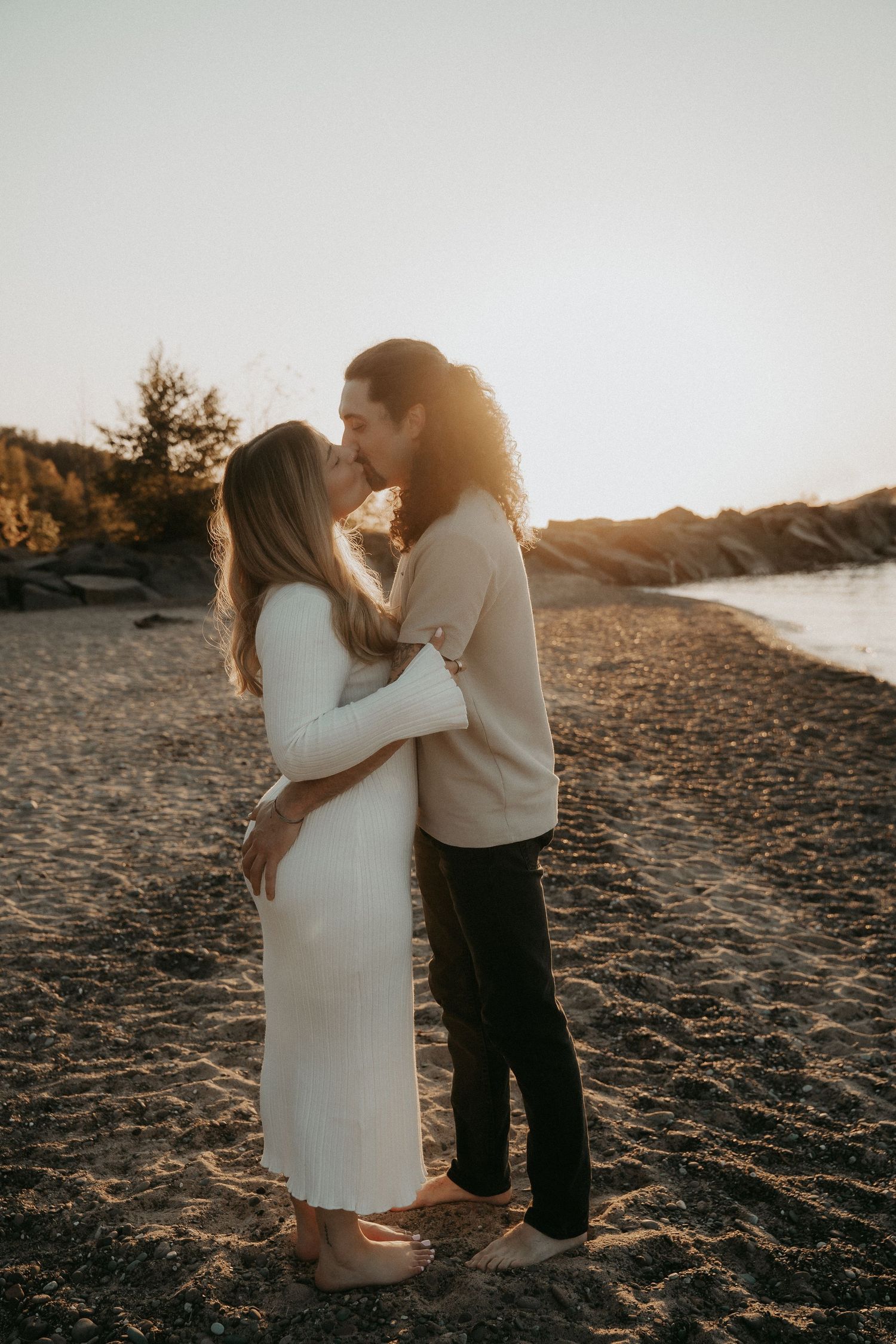 A couple embraces on a sandy beach at sunset creating a romantic silhouette against the golden light.