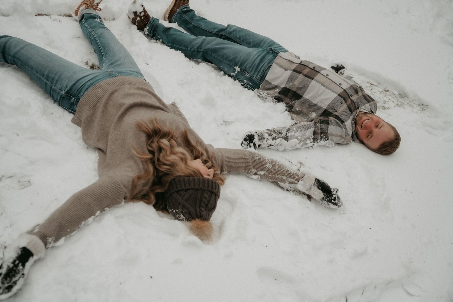 Person lying in snow wearing winter clothing and boots, creating snow angels in a playful winter scene.