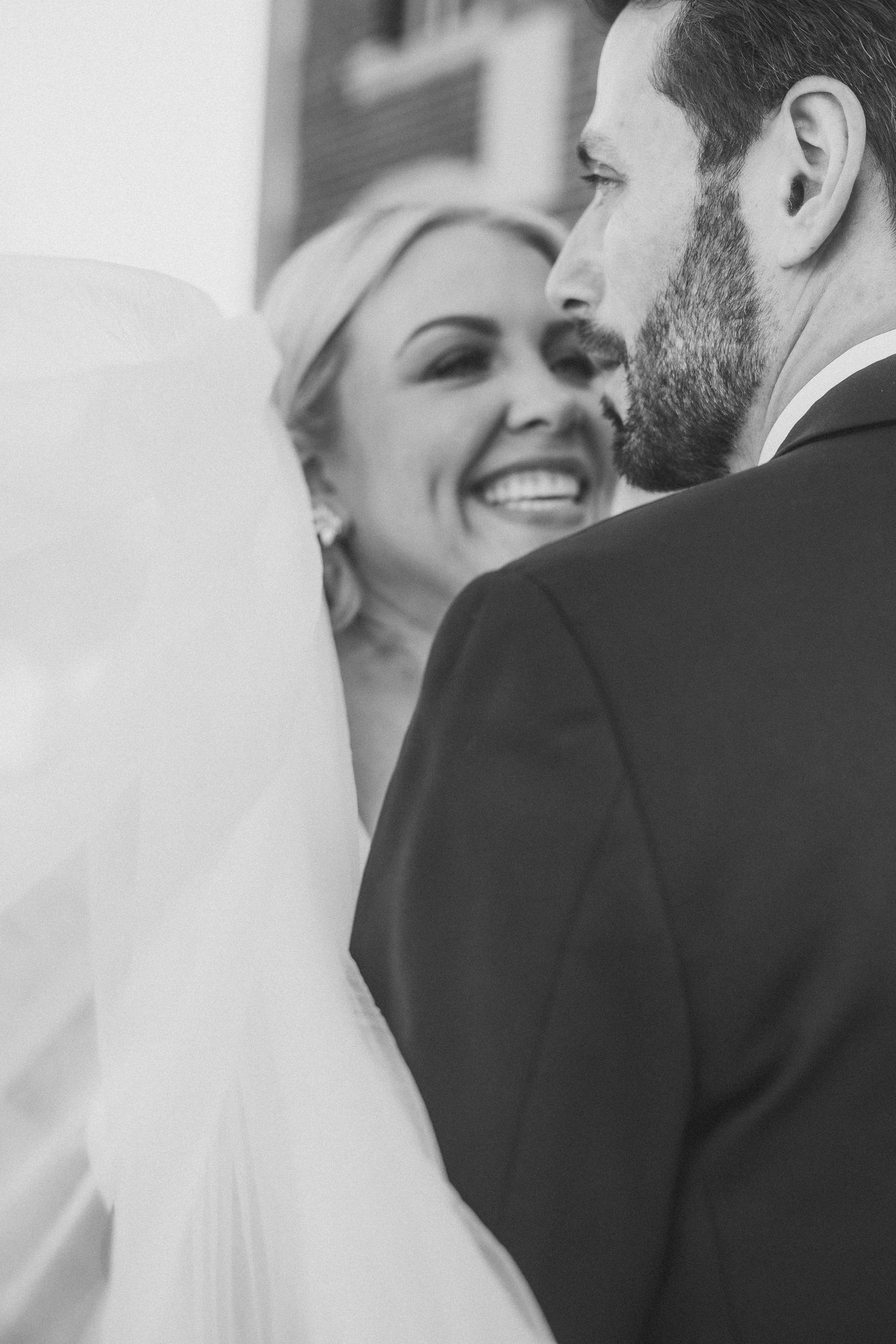 Black and white romantic wedding portrait capturing a tender moment through a flowing veil.