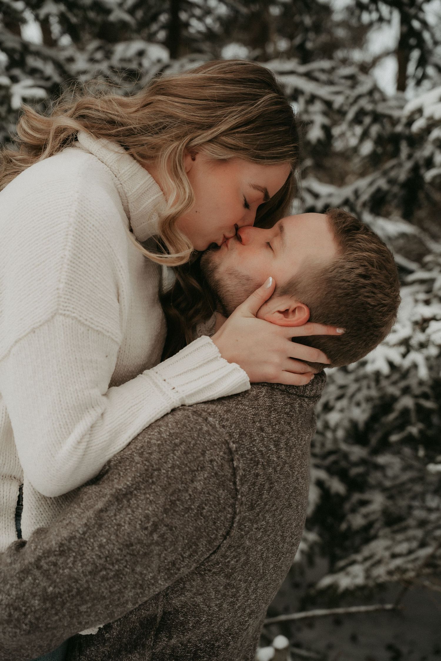 A romantic winter scene shows a couple in white and brown sweaters sharing an intimate moment against a snowy backdrop.