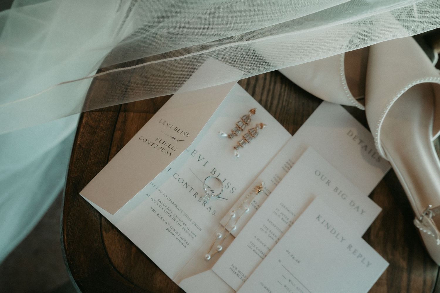 Wedding invitation suite with white envelopes and elegant calligraphy laid out on dark wooden surface.