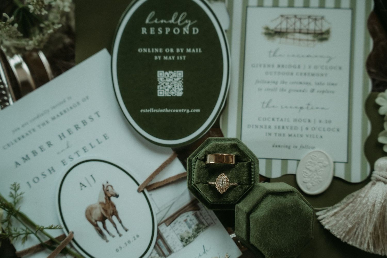 Elegant wedding stationery flat lay featuring green velvet ring box, gold rings, RSVP card with QR code, and horse illustration.