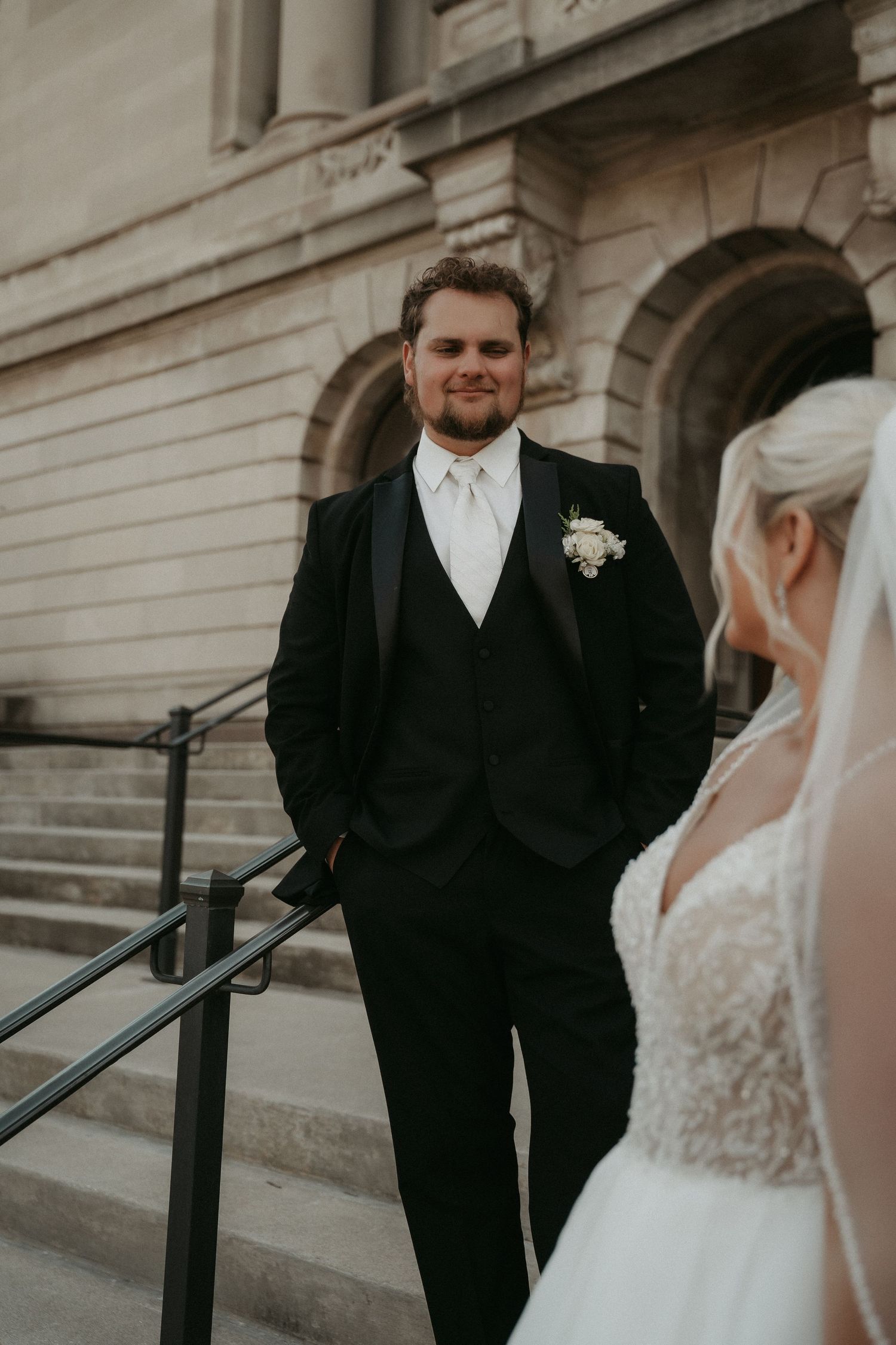 First look wedding photos showing couple in formal attire sharing intimate moments on stone steps of historic building.