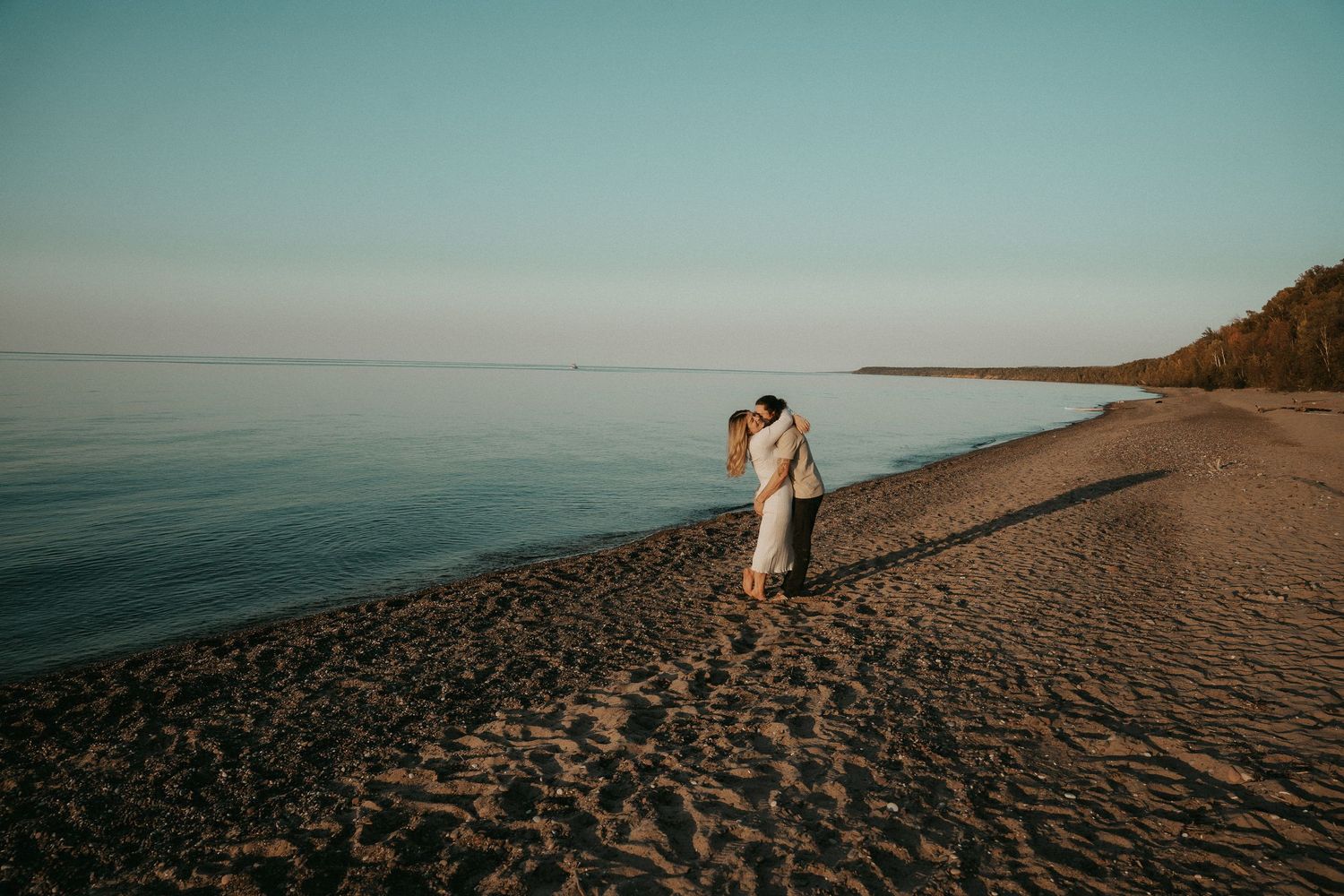 A couple shares a romantic moment at sunset on a pristine beach with golden light illuminating the shoreline.