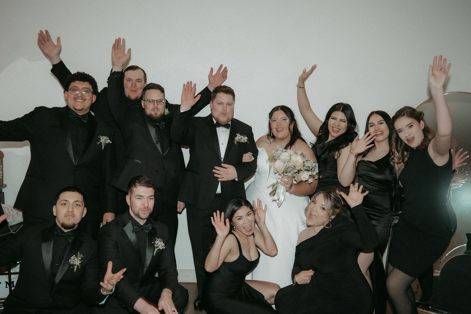 Large group of people with raised hands celebrating and posing together in a casual indoor setting.