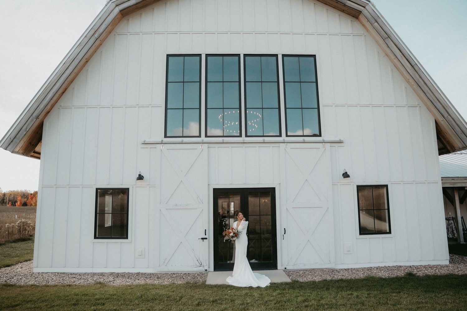 Modern white barn with sleek black windows and doors set against a cloudy sky in a minimalist architectural style.