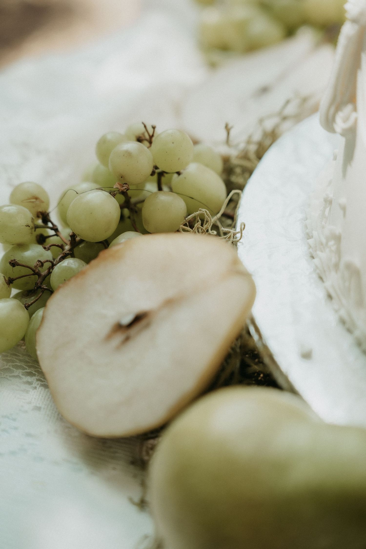 Close-up of fresh green grapes and sliced pear arranged on a white lace surface with soft natural lighting.