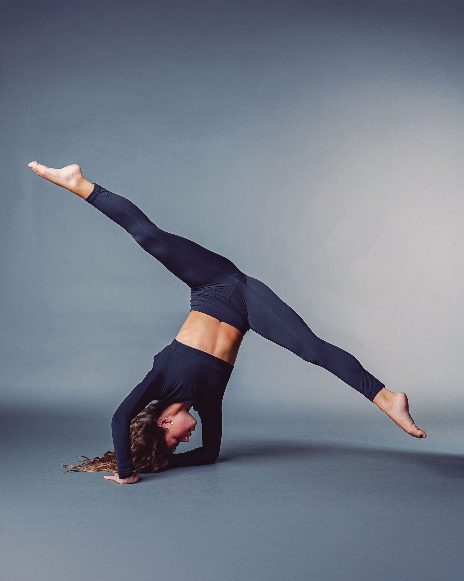 A dancer in black attire performs a graceful sequence of movements against a gray studio backdrop.
