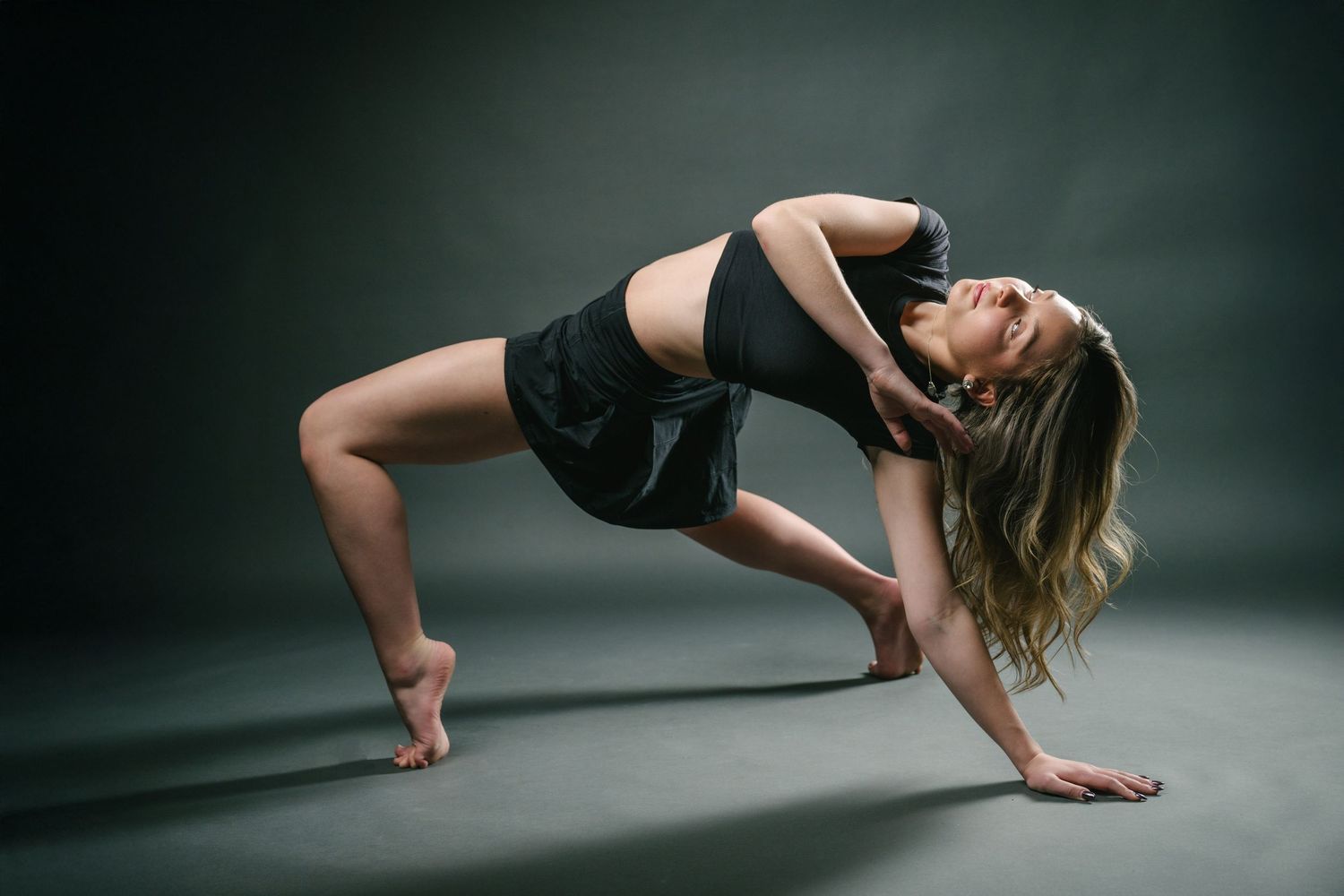 A dancer performs a graceful contemporary dance sequence in a dark studio with dramatic lighting.