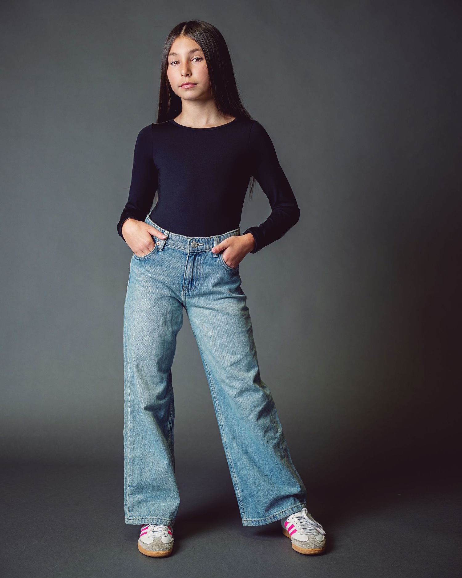 A series of fashion portraits showing a model in a black long sleeve top and wide-leg light wash jeans against a gray backdrop.