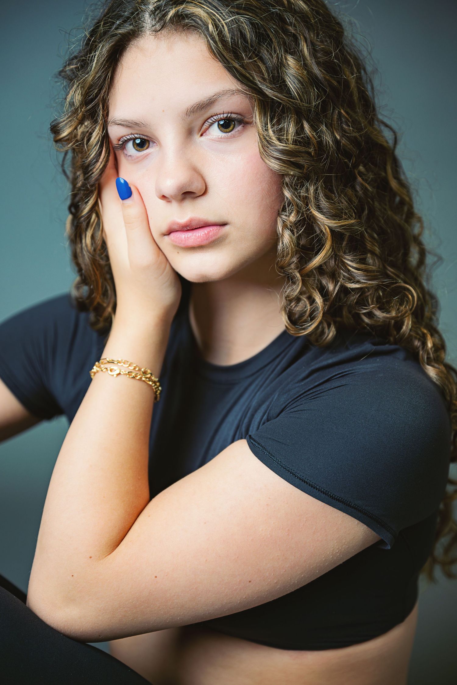 A series of artistic portrait photographs showing curly hair and blue nail polish against a dark studio backdrop.
