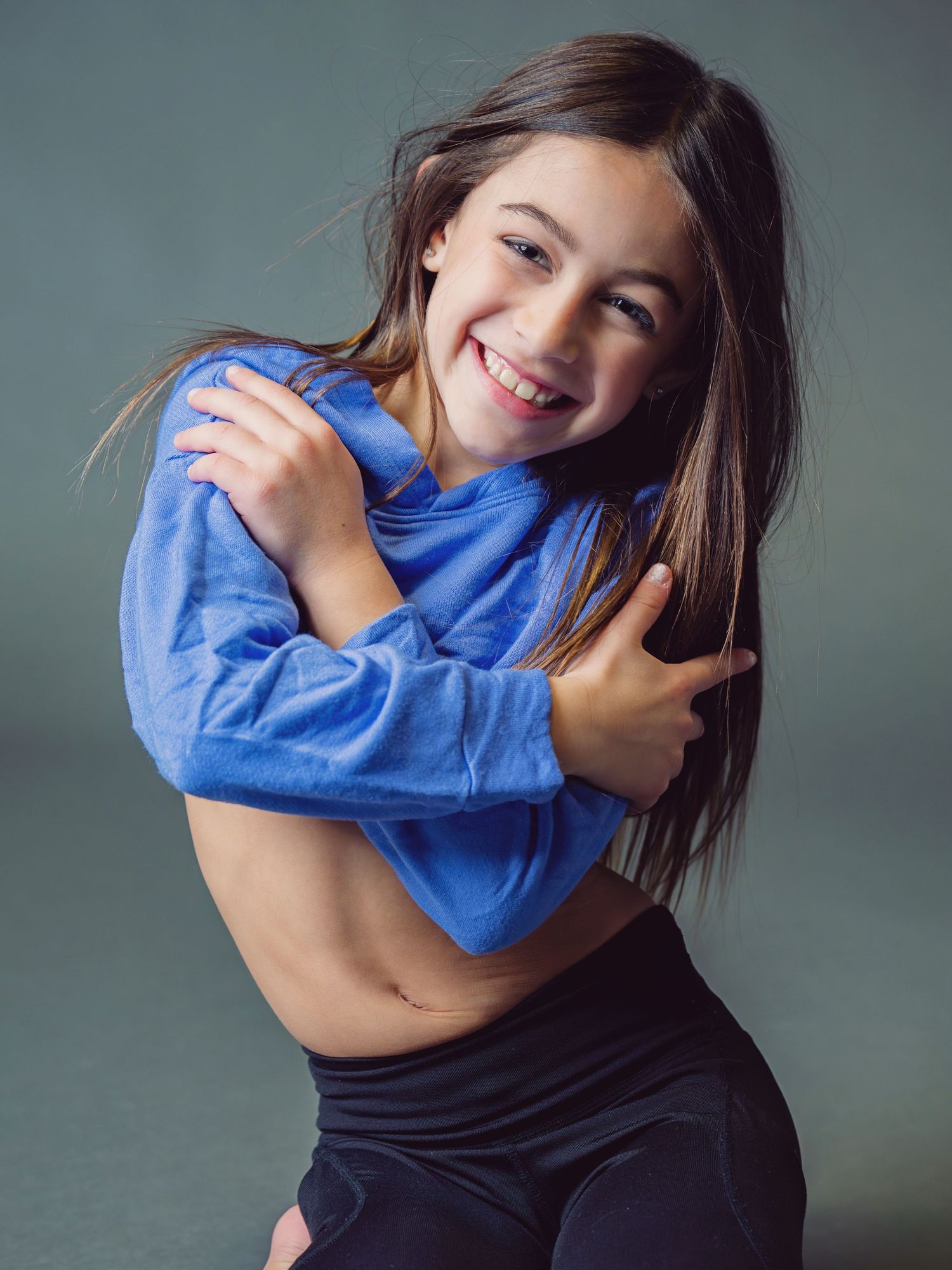 Person in blue sweater making playful expressions against grey background.