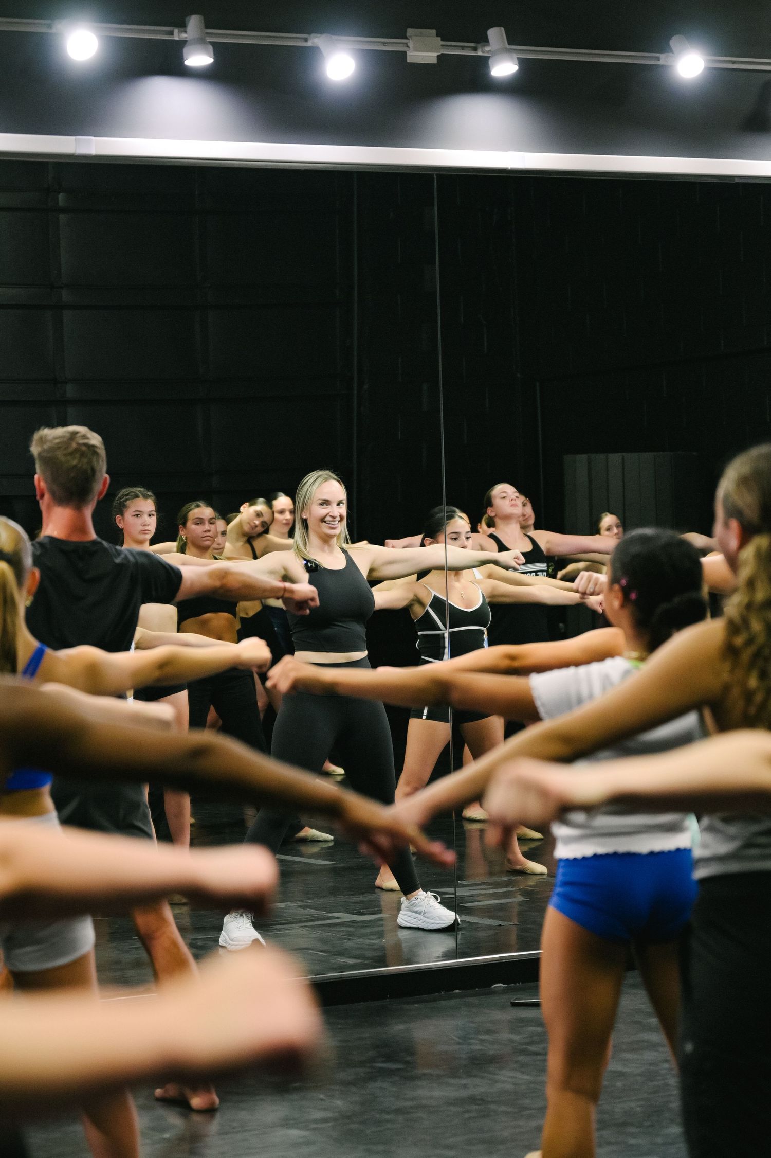 Dancers in a mirrored studio perform synchronized arm movements during a group dance class.