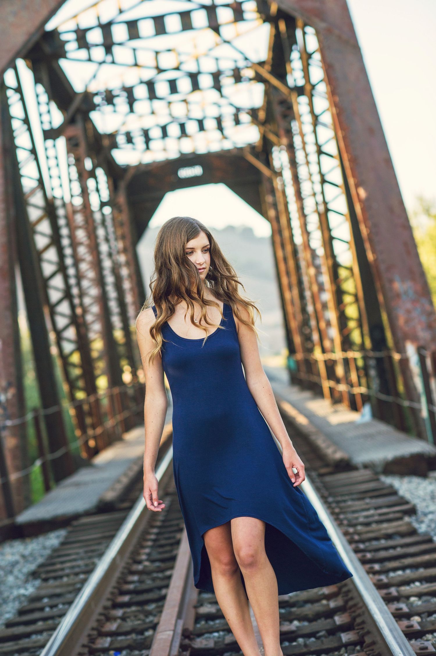 Stylish blue dress photographed on rustic railroad tracks with an old iron bridge in background.