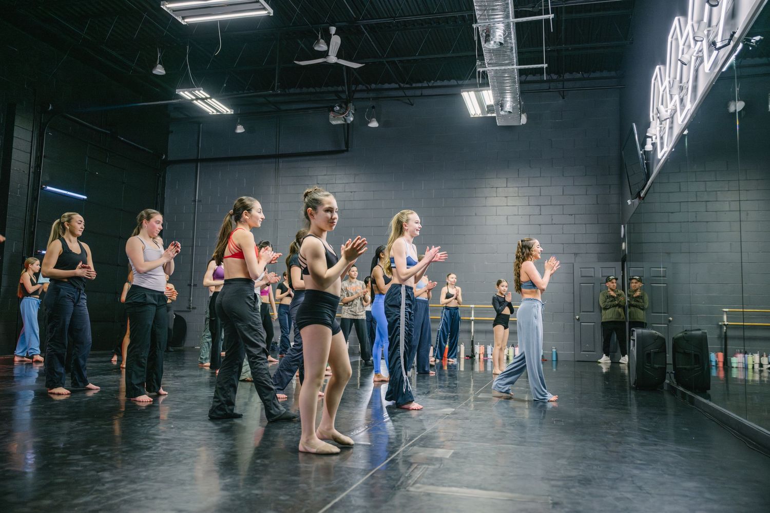 Dance students practice in sync during a contemporary dance class in a dark studio space.