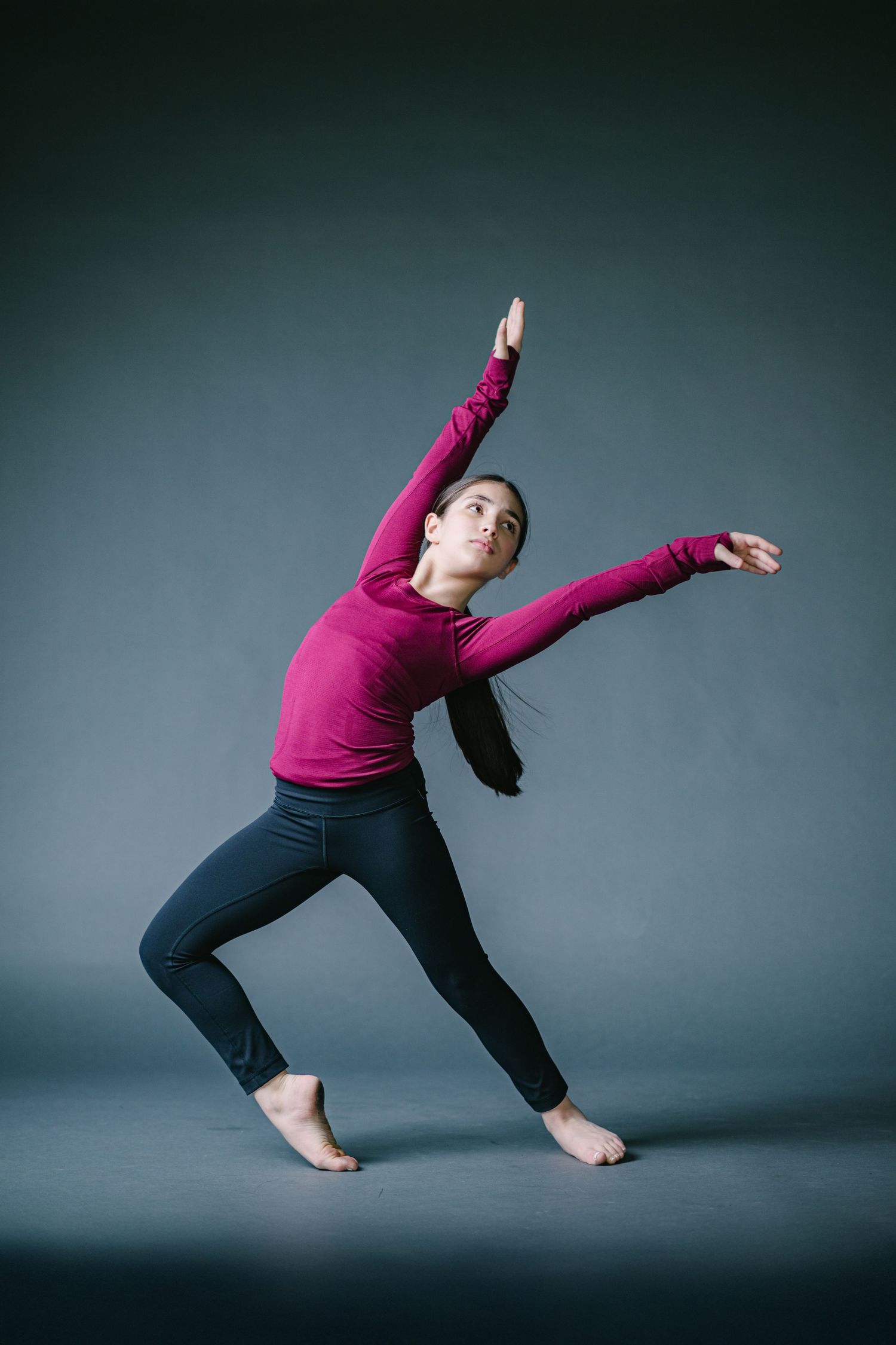 Dancer in magenta top and dark pants moves gracefully in a contemporary dance sequence against grey background.