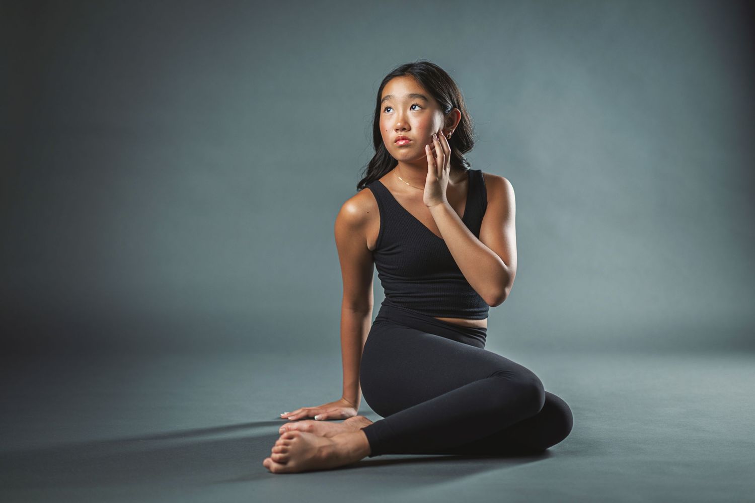 Athletic figure in black workout attire performs yoga stretches and poses on gray studio floor.