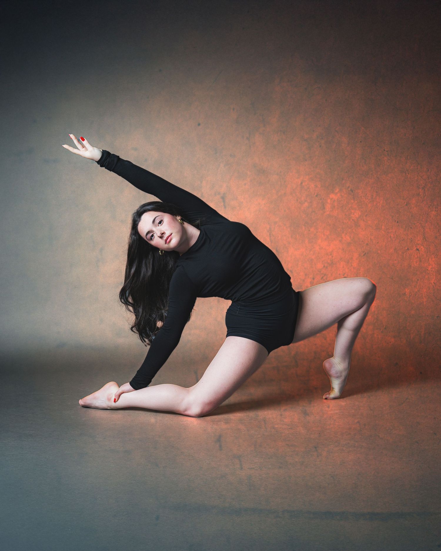 A dancer in black leotard performs an expressive contemporary dance sequence on a textured orange-lit floor.