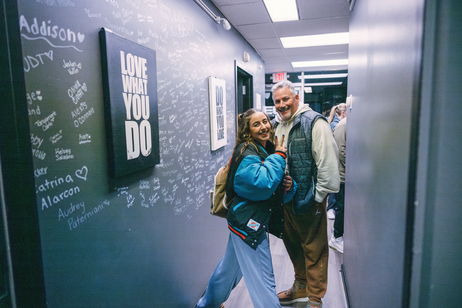 People gather in a studio hallway with inspirational quotes written on gray walls.