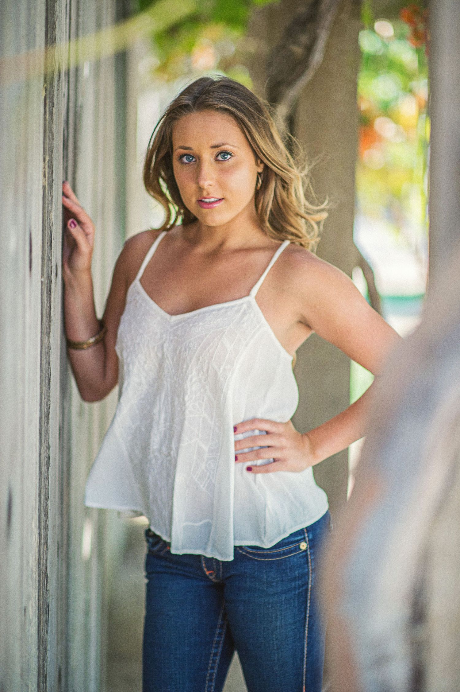 Casual summer fashion portrait with white flowy tank top and jeans against rustic door frame.