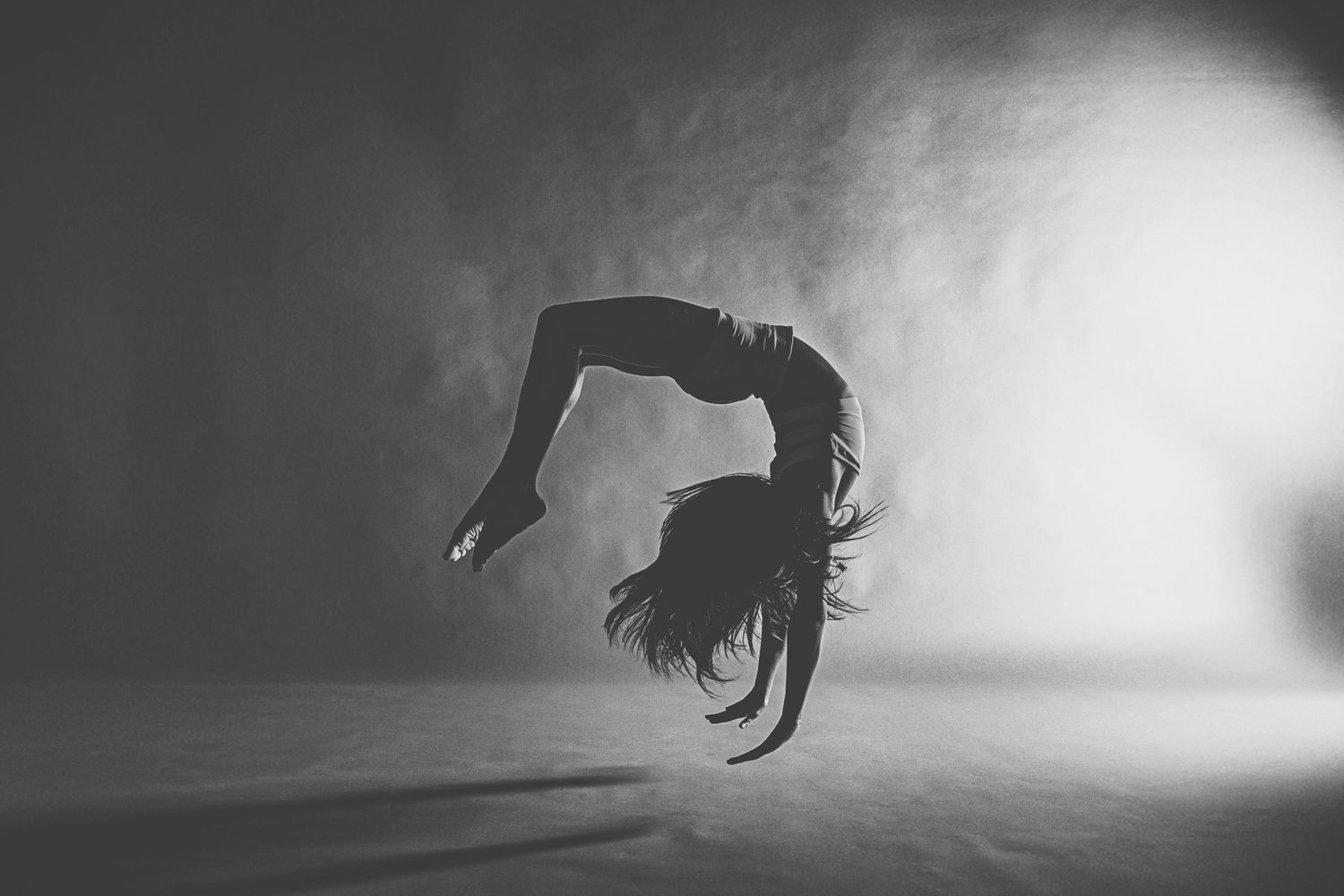 A dramatic sequence of silhouetted figures performing backflips and acrobatic movements against a light background.