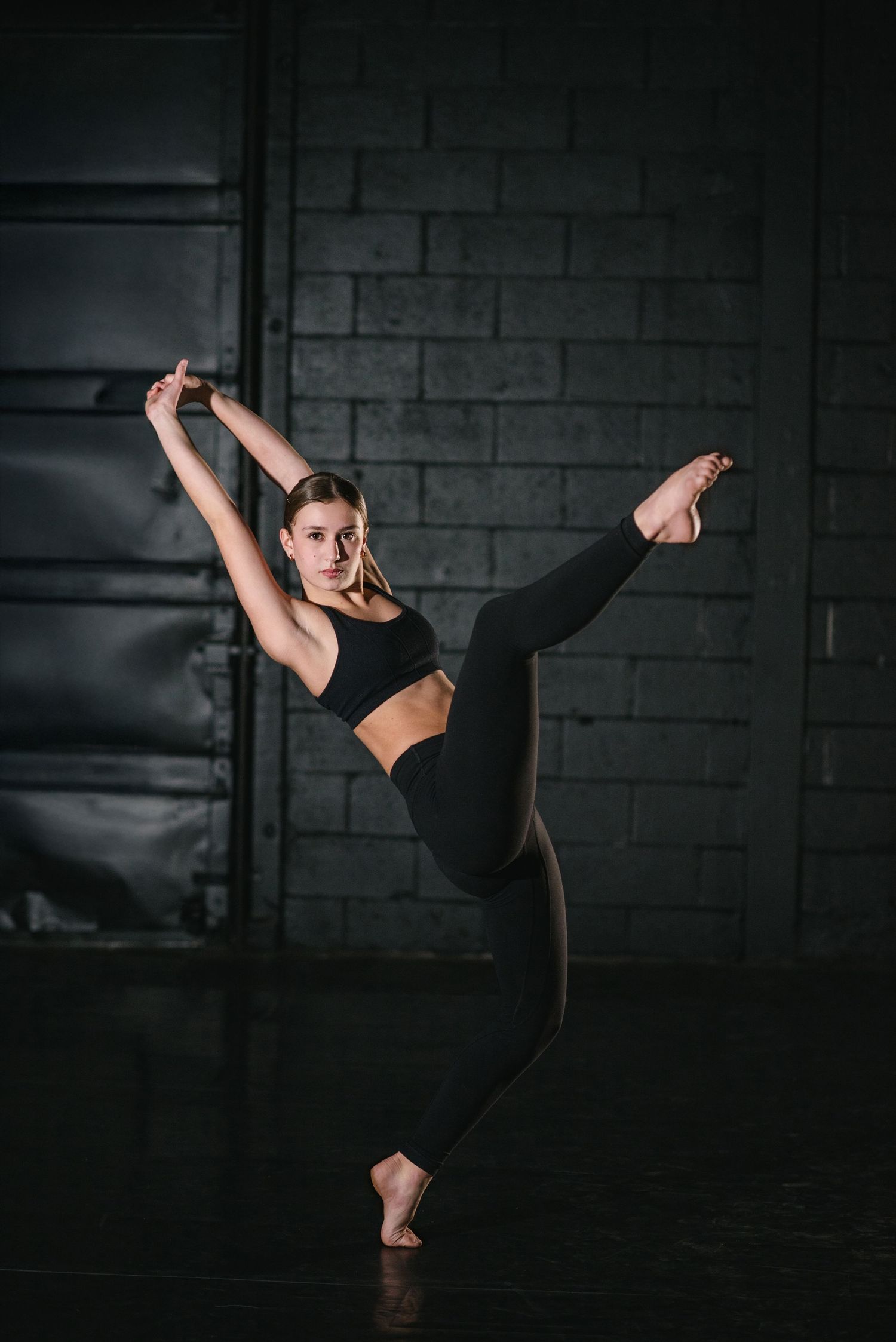 Athletic dancer performs dynamic high kick sequence in dark studio against concrete wall backdrop.