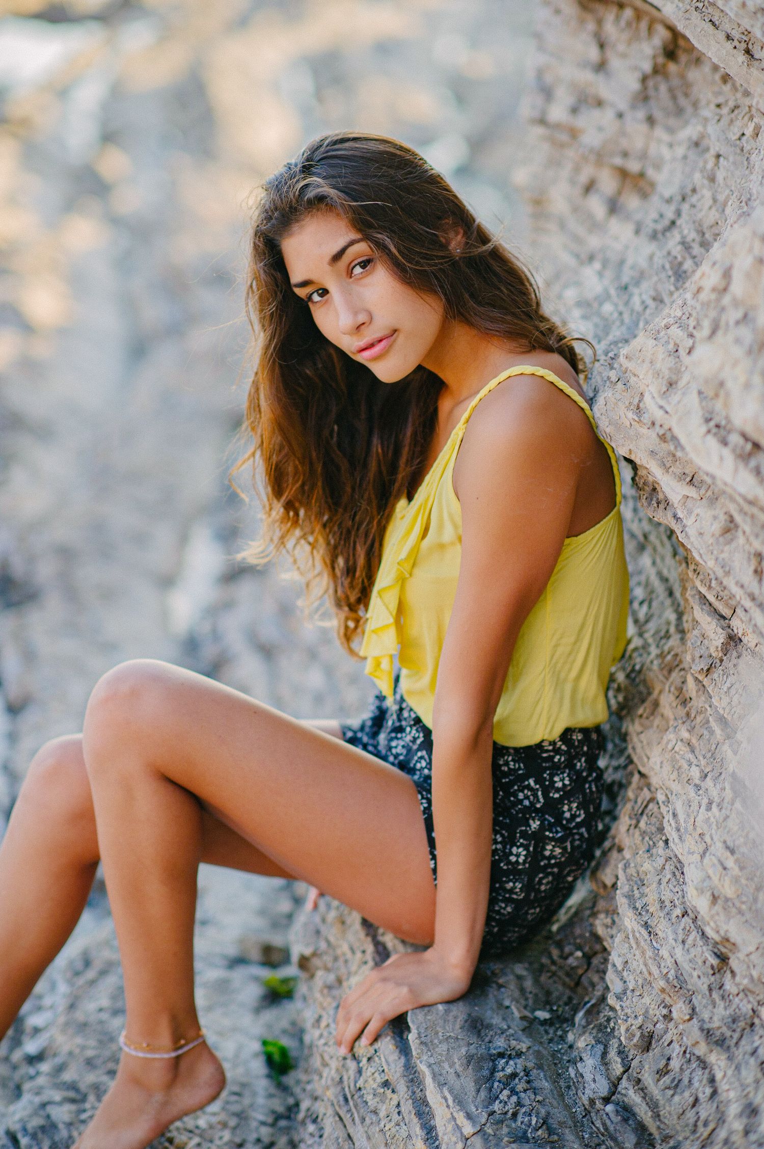 A woman in a yellow top and dark shorts poses gracefully against a rocky cliff in a series of artistic outdoor portraits.