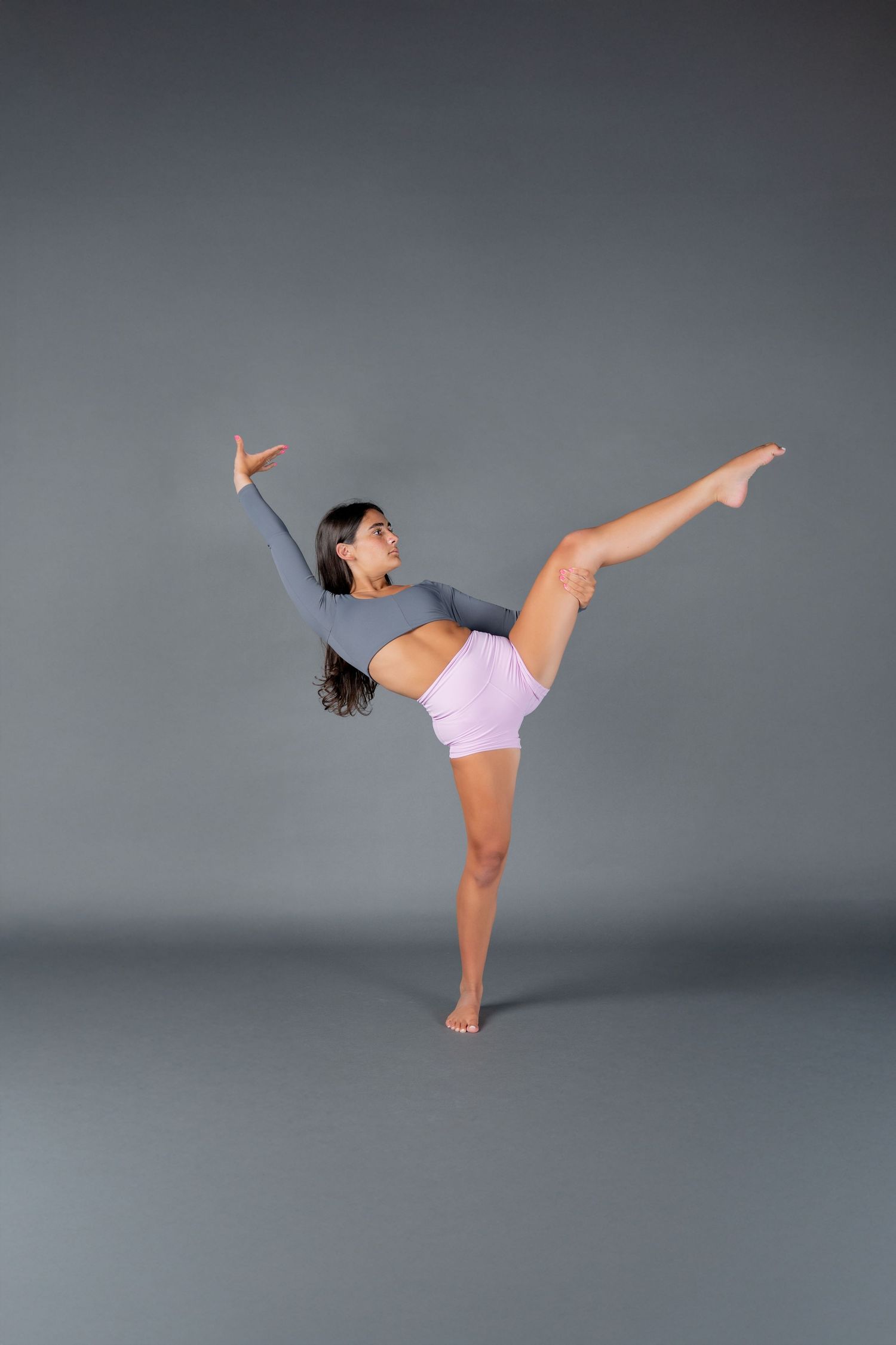 A dancer performs a graceful high kick sequence in a pink top and shorts against a gray studio backdrop.