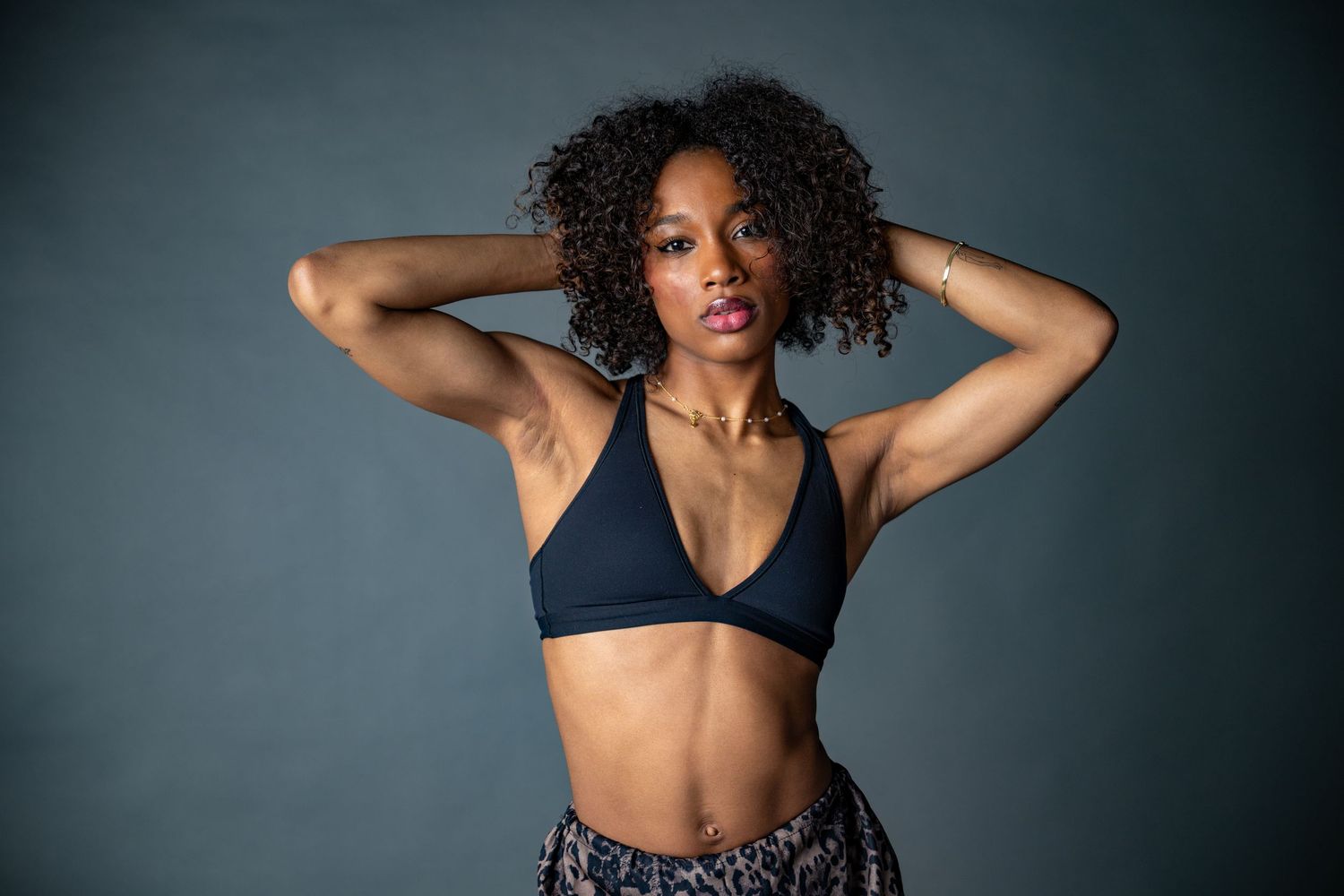 Athletic woman with curly hair performs dynamic fitness poses in dark studio setting against grey background.
