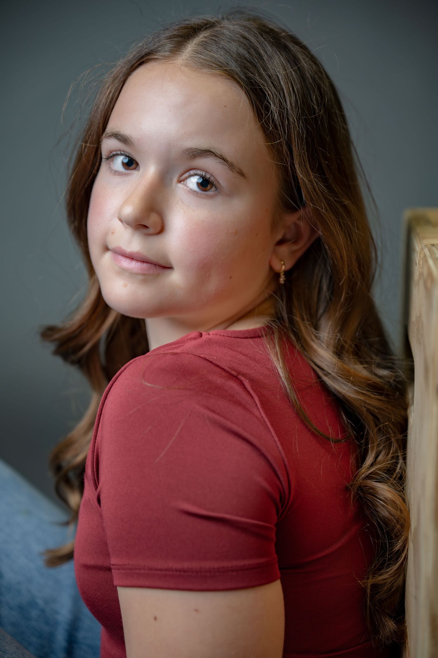Portrait of a young person in a red short-sleeved top looking over their shoulder with long wavy brown hair.