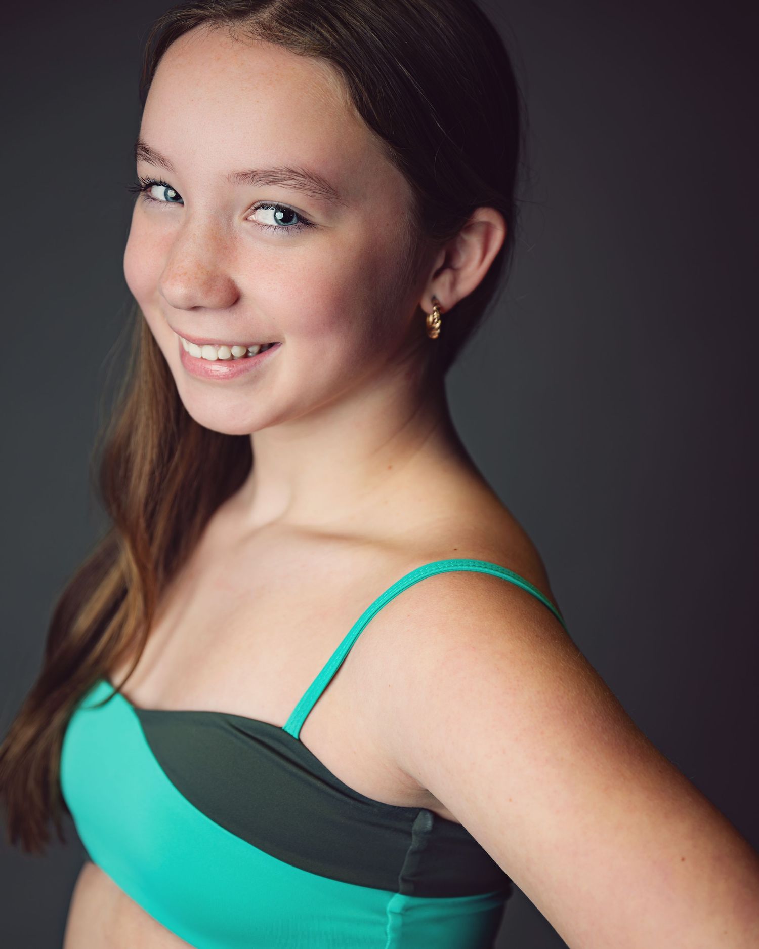 Portrait of dancer in turquoise dance attire against dark background with soft studio lighting.