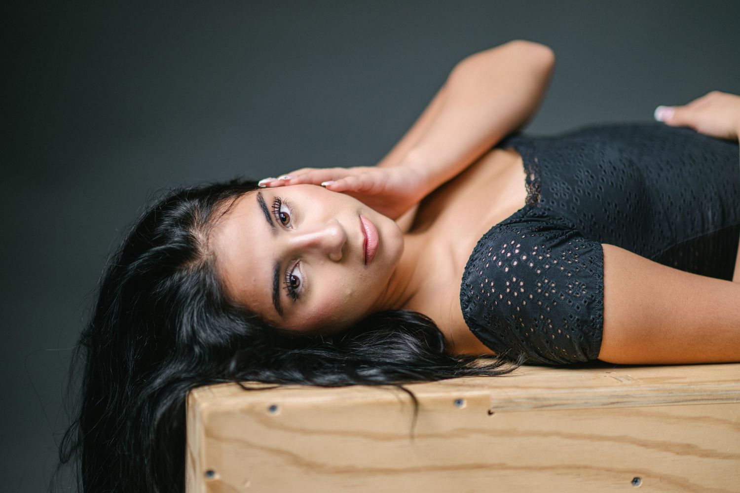 A woman in black lingerie poses seductively on a bed with dramatic lighting and shadows.