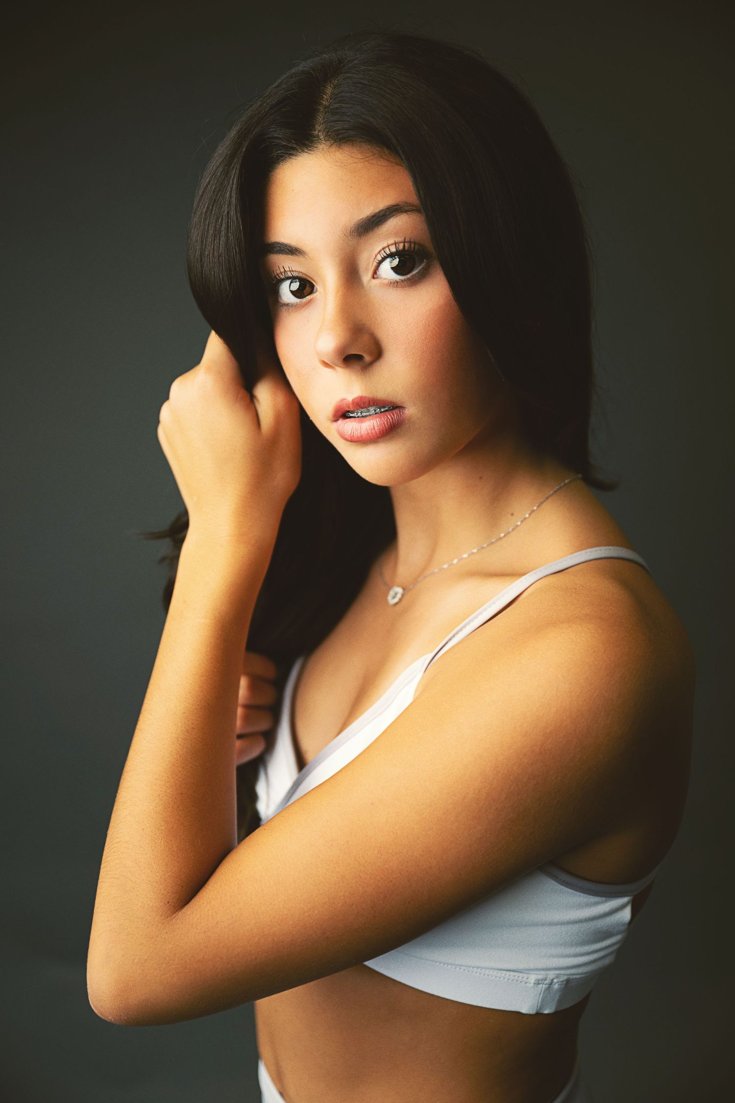 Studio portrait of a person in a white tank top posing against a dark background with dramatic lighting.
