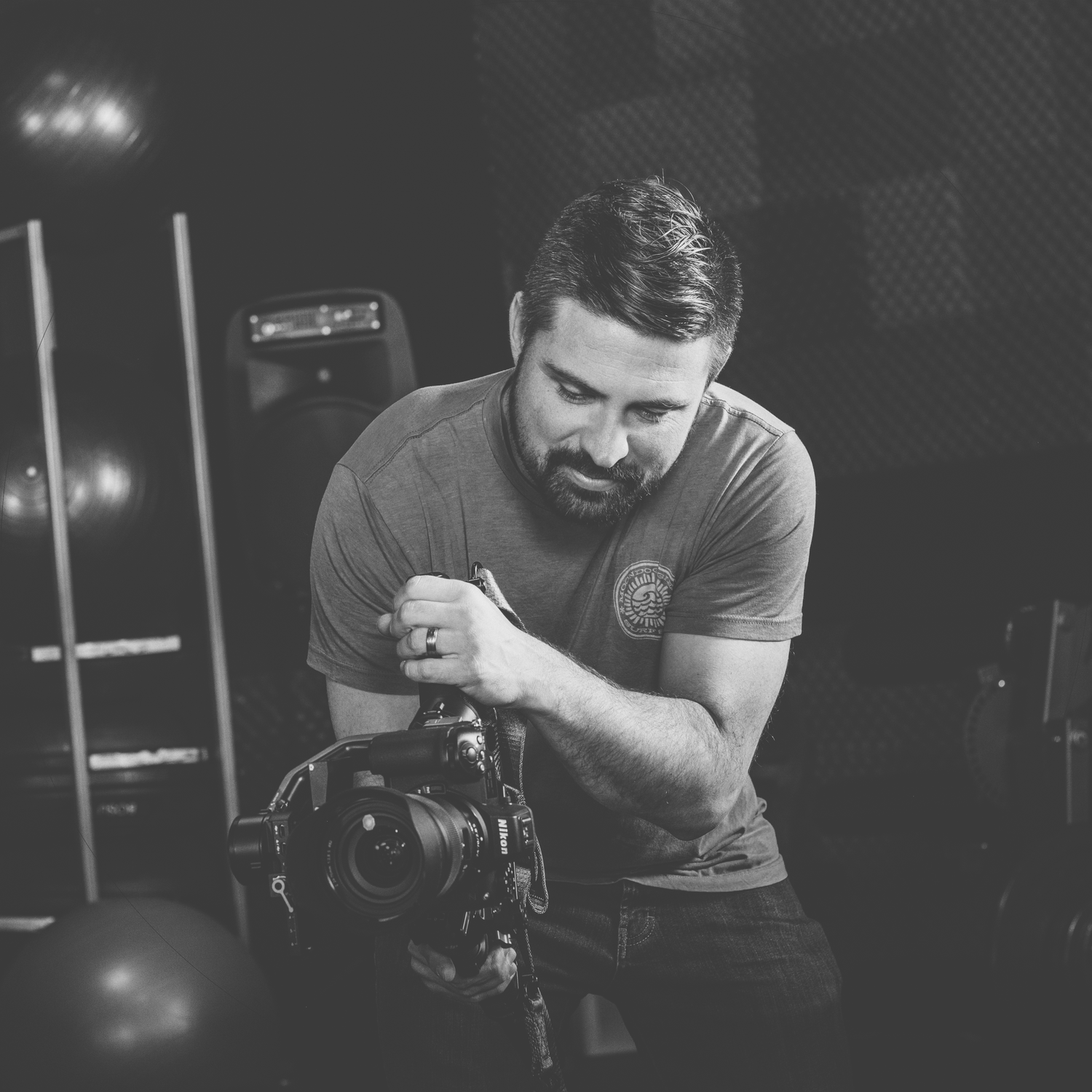 Black and white portrait of photographer working with camera equipment in low light.