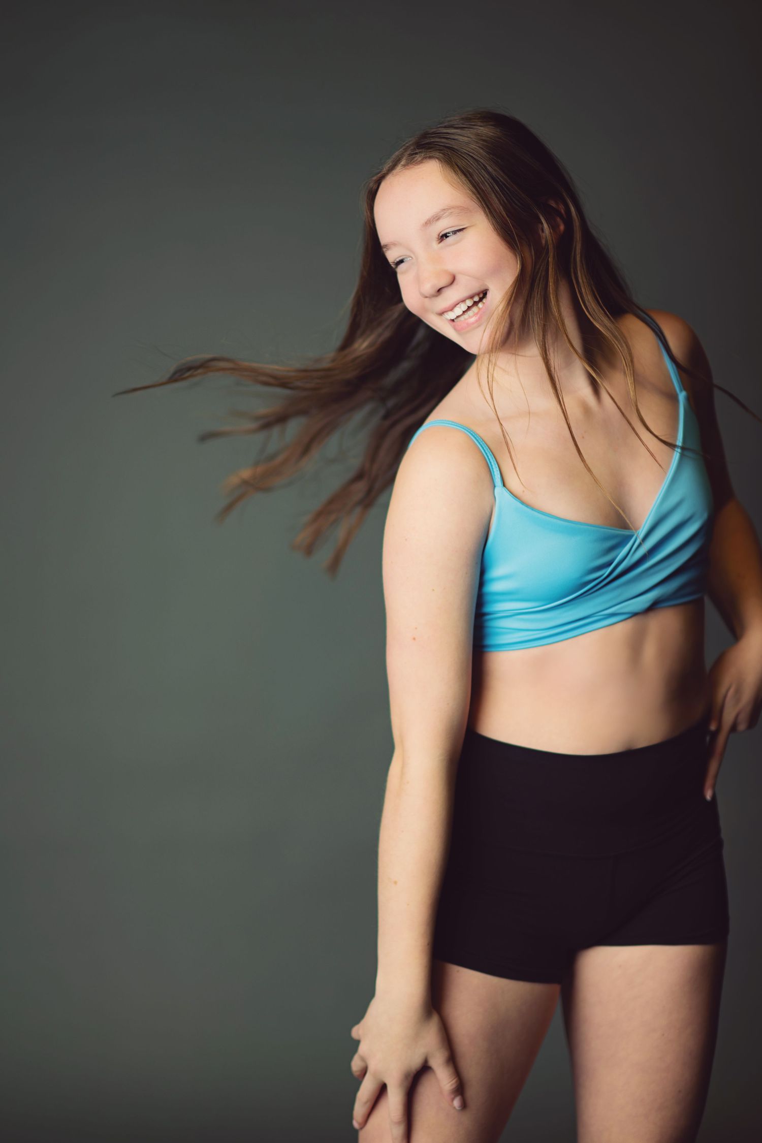 Dancer in blue top and black shorts creates dynamic movement with flowing hair against dark background.