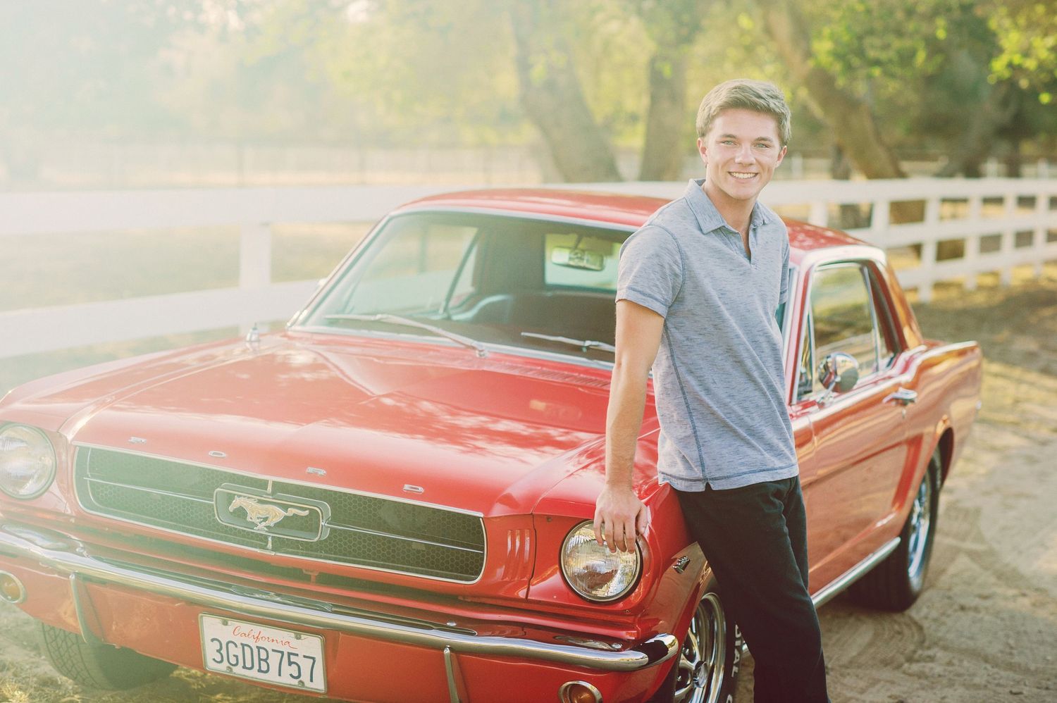 A vintage red Ford Mustang convertible parked in a scenic outdoor setting during golden hour.