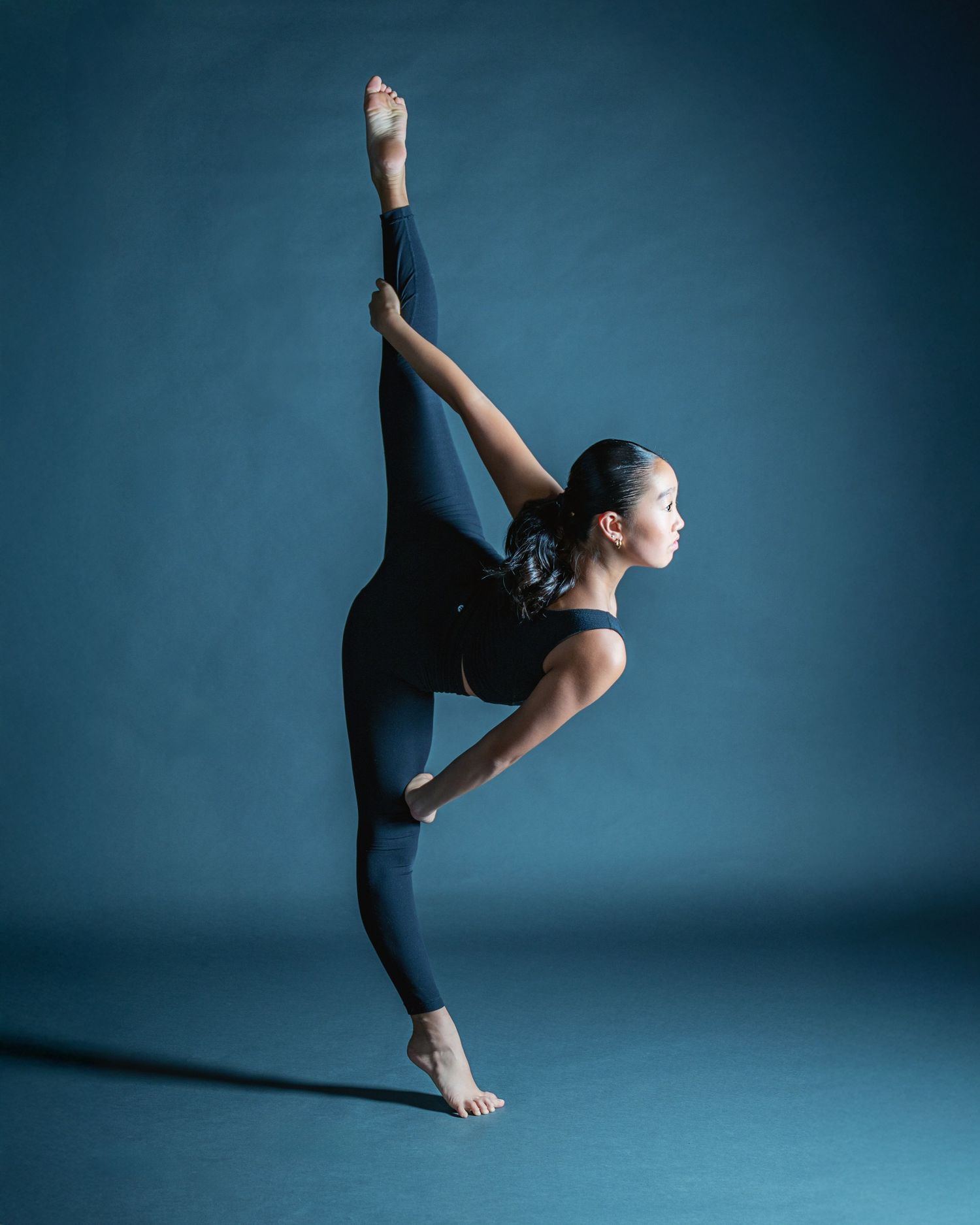 A dancer performs a dramatic high kick against a moody blue backdrop in a series of graceful movements.