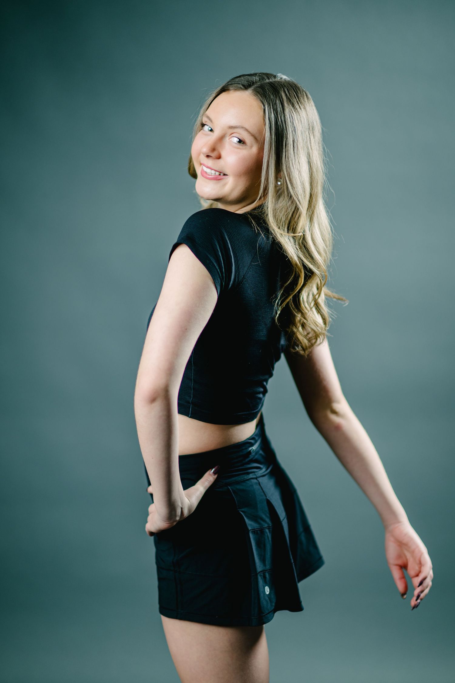 A figure in a black dress twirls and poses dynamically against a teal studio backdrop in a sequence of motion shots.