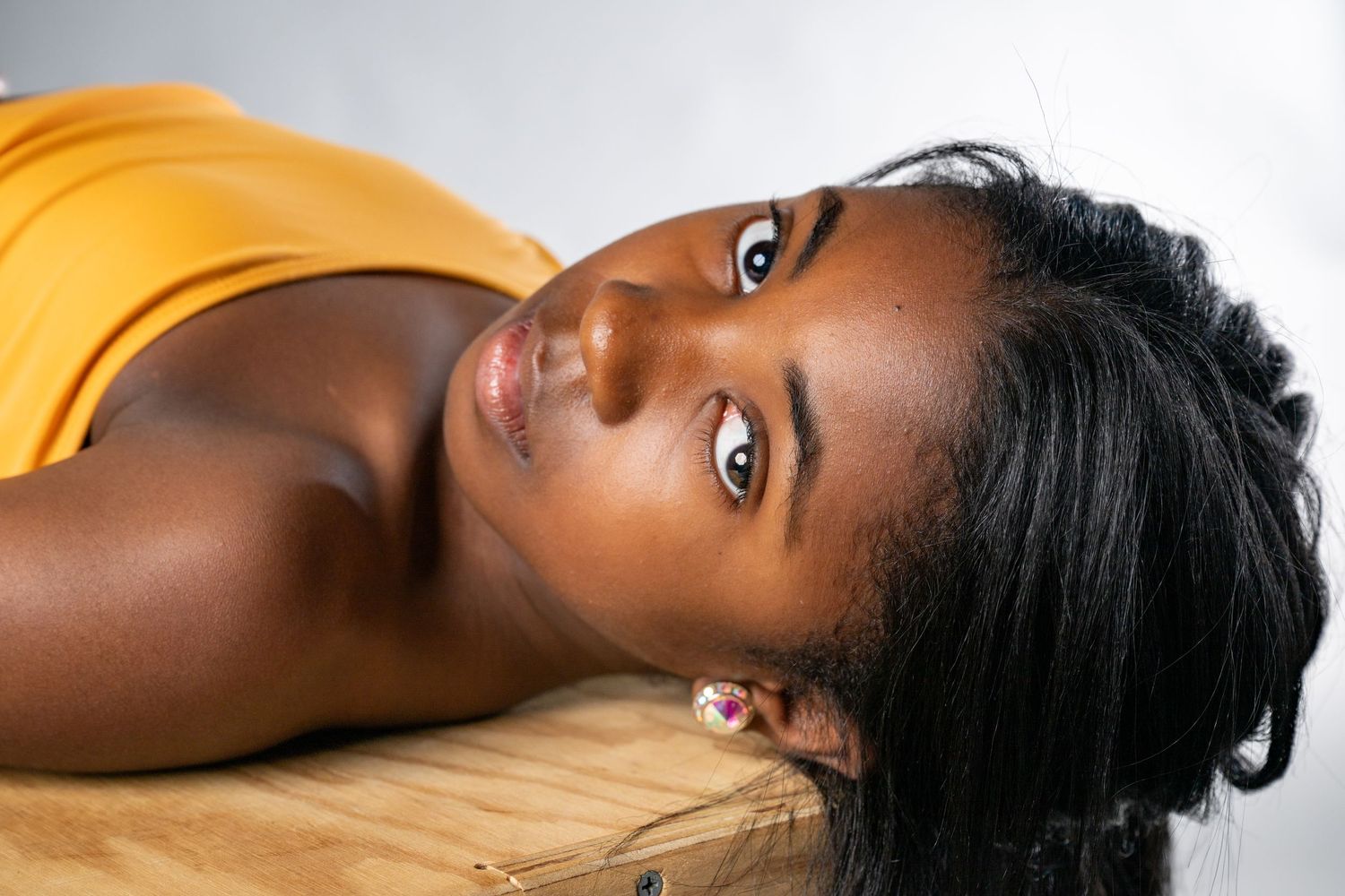 A person with dark hair rests their head on a wooden surface while wearing a yellow top.