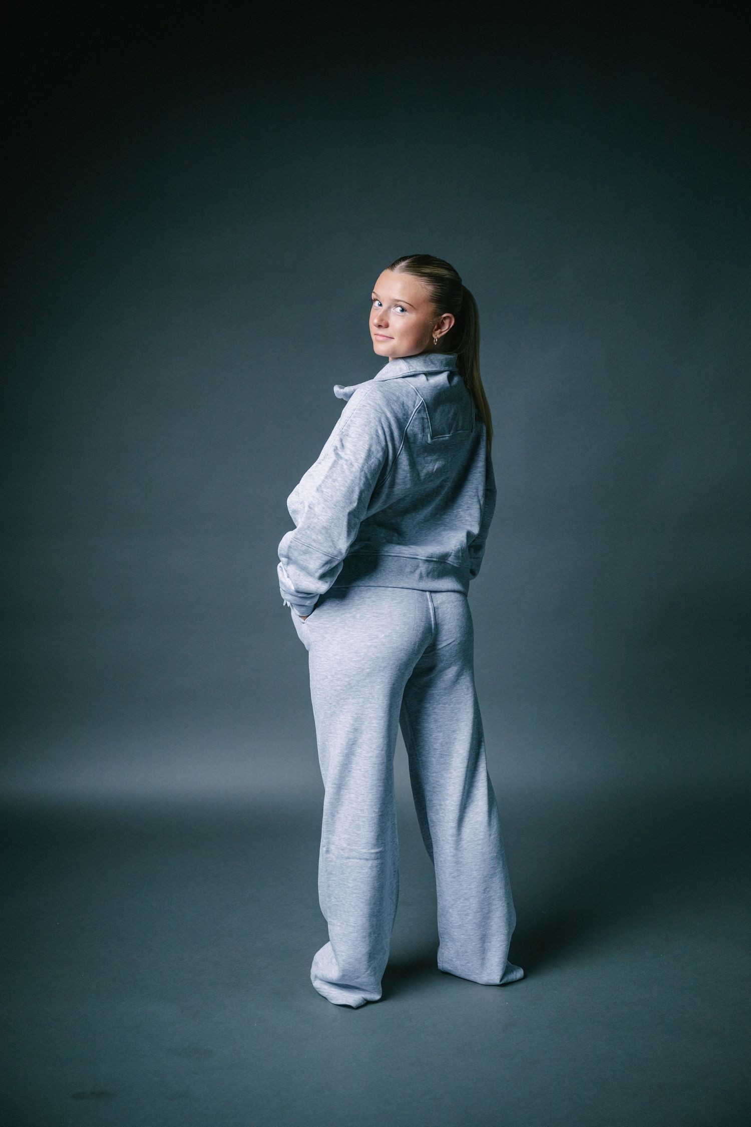A person wearing an oversized grey sweatsuit poses in various angles against a dark studio backdrop.
