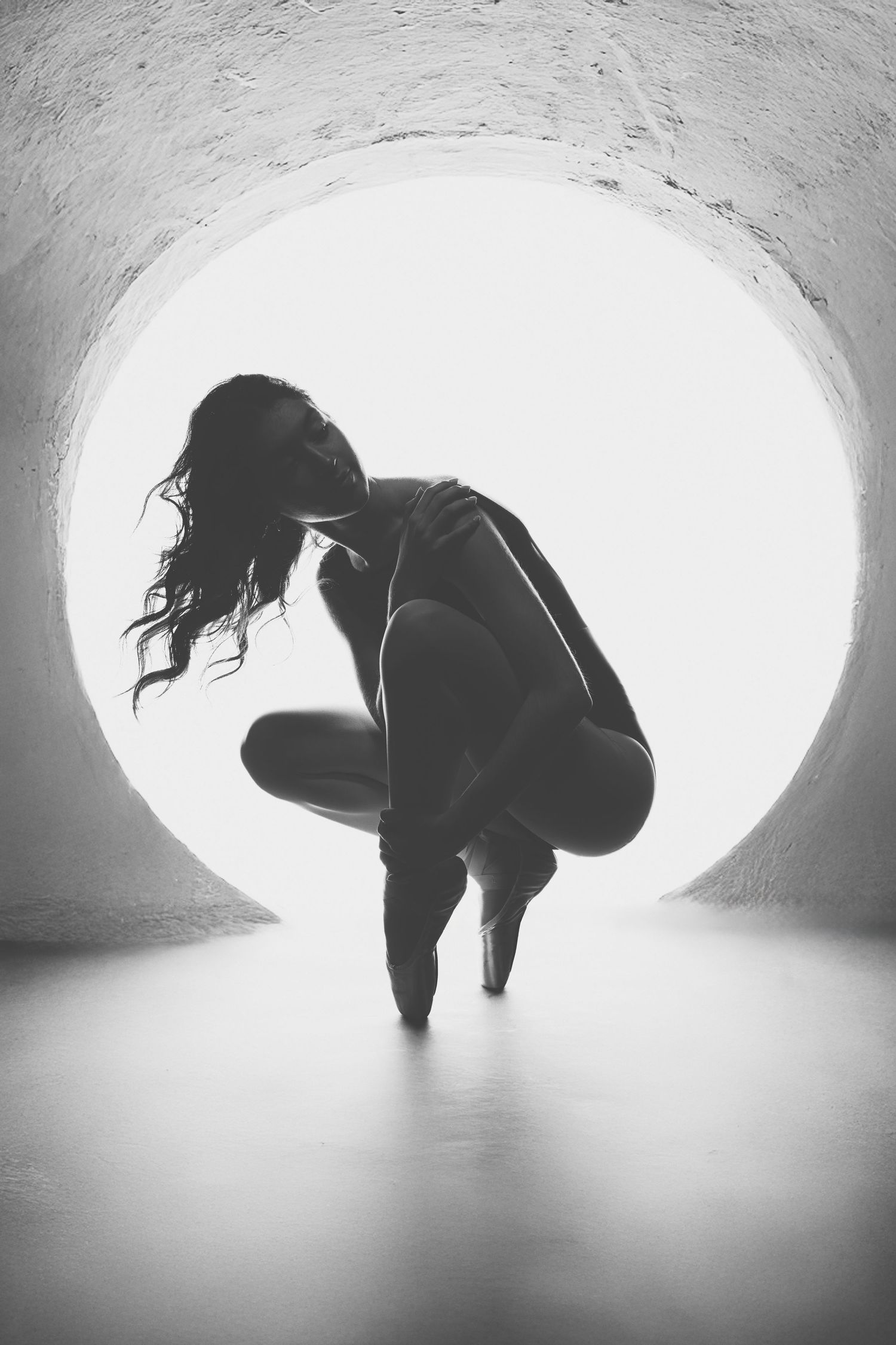 Silhouetted figure performing expressive dance movements in a curved white tunnel space.